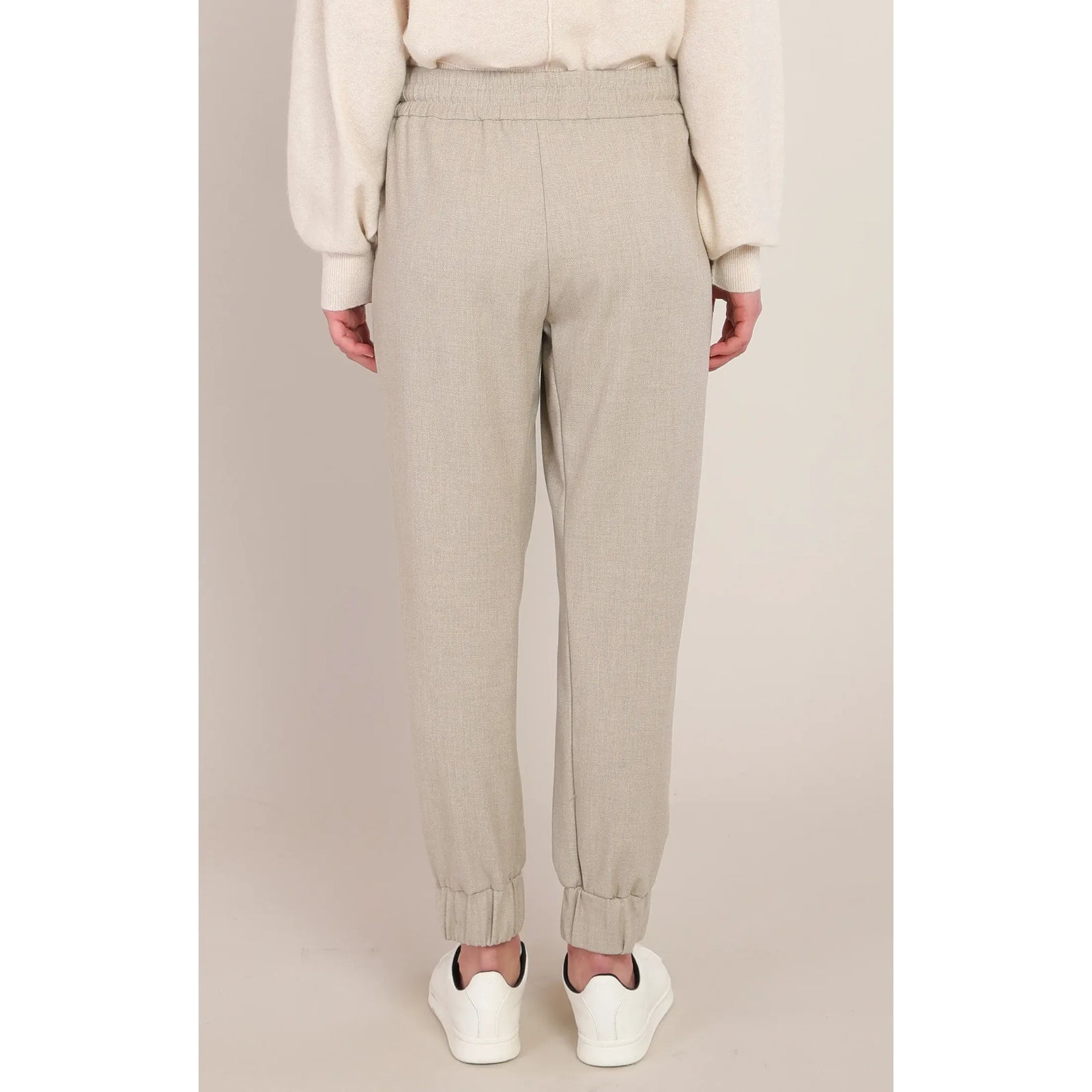 Back view of beige cuffed hem knit pants with a relaxed fit and elastic waistband, styled with white sneakers.