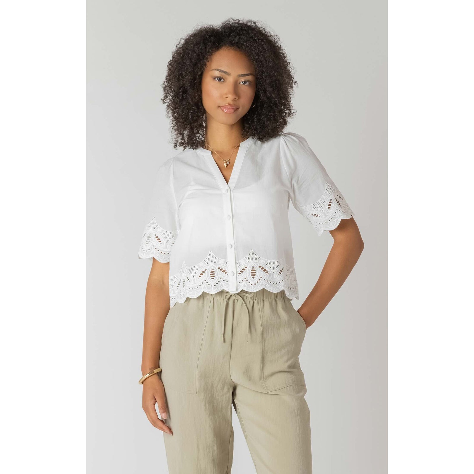 Room 34 Eyelet Trim Blouse: white short-sleeve top with scalloped eyelet hem on model, beige pants.