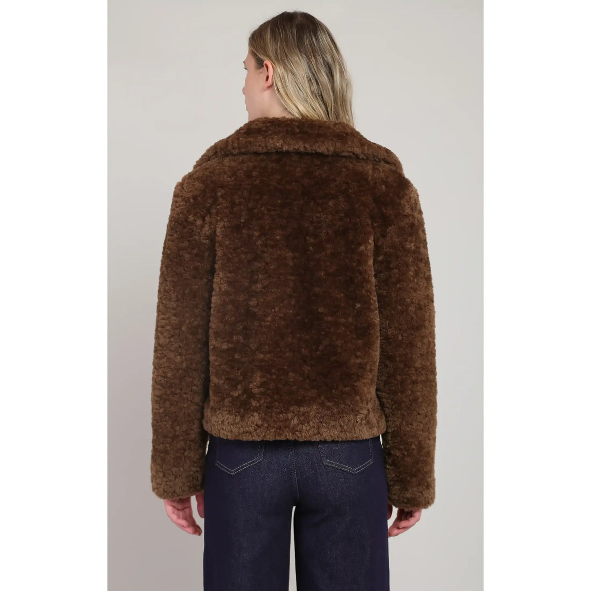 Back view of arich brown faux fur coat featuring a plush texture, wide collar, and cropped fit paired with dark denim.