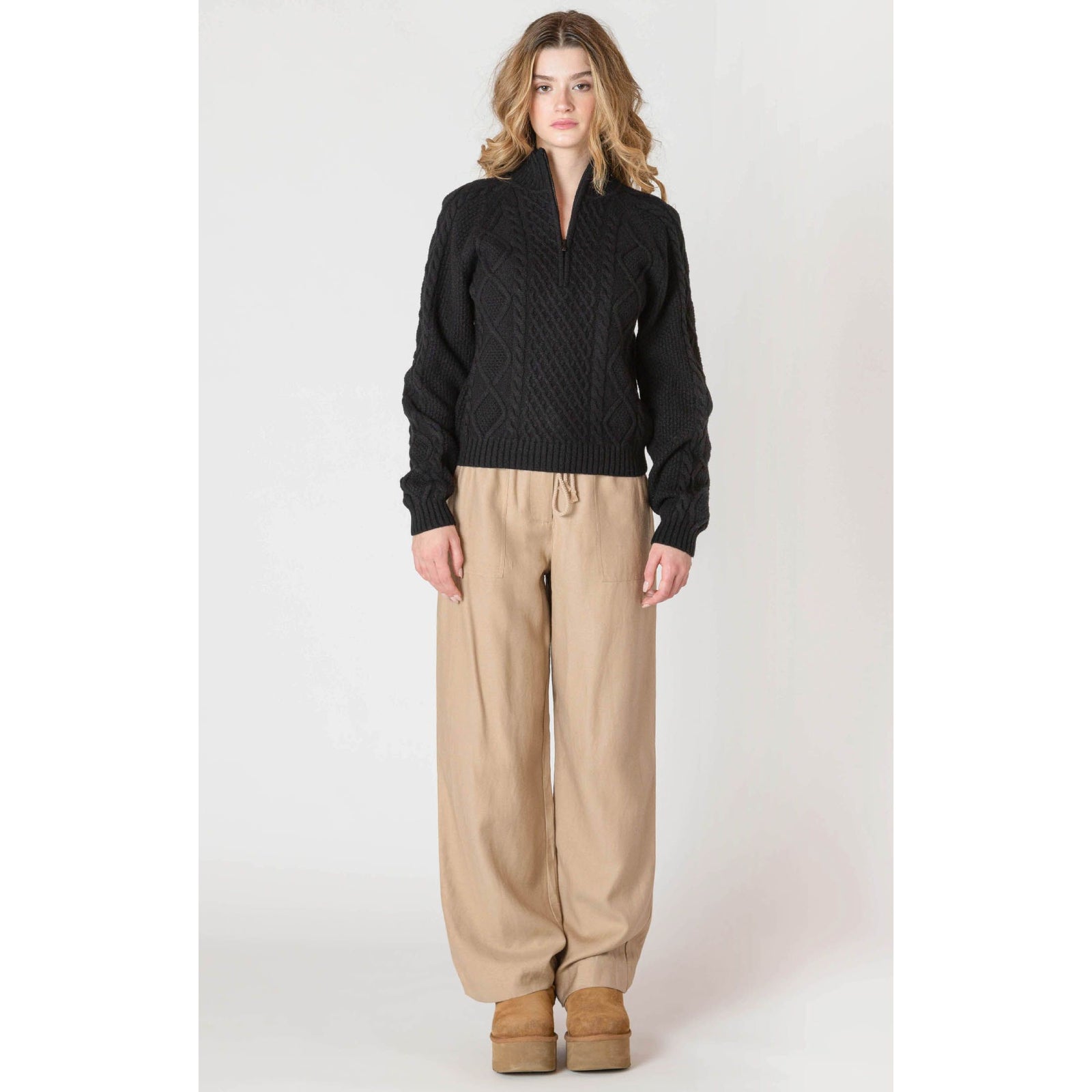 Room 34 Half Zip Cable Knit Sweater in black with classic cable knit, worn with beige wide-leg pants.