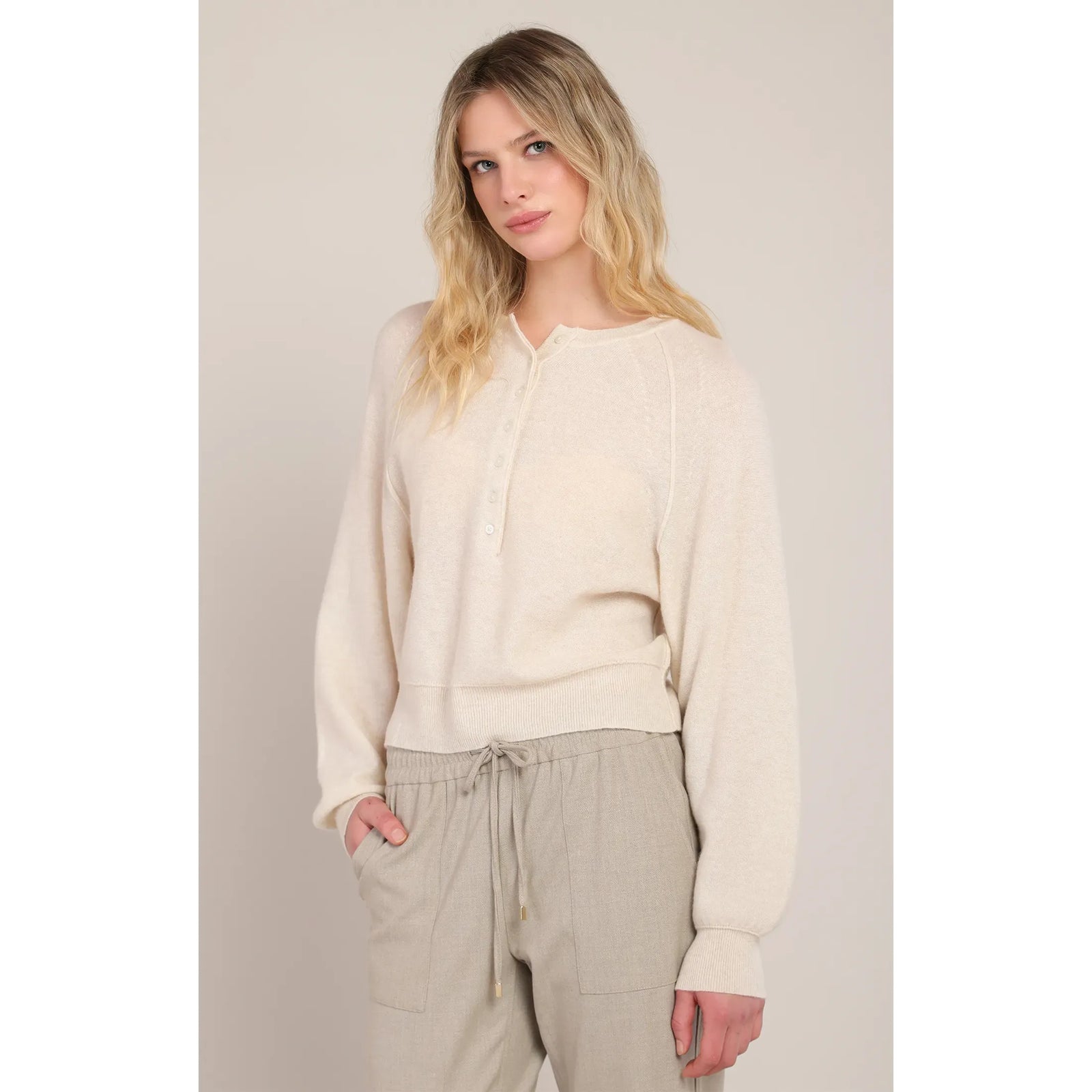 Cream henley sweater with button placket and ribbed hem, styled with grey joggers for effortless everyday comfort and layering.