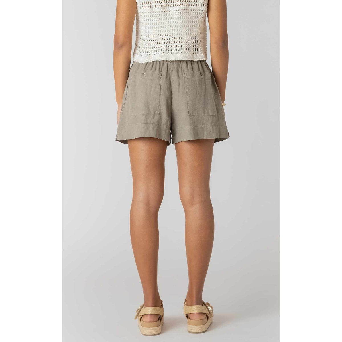 Back view of model wearing Room 34 Mid-rise Shorts in taupe, woven fabric with two back pockets.