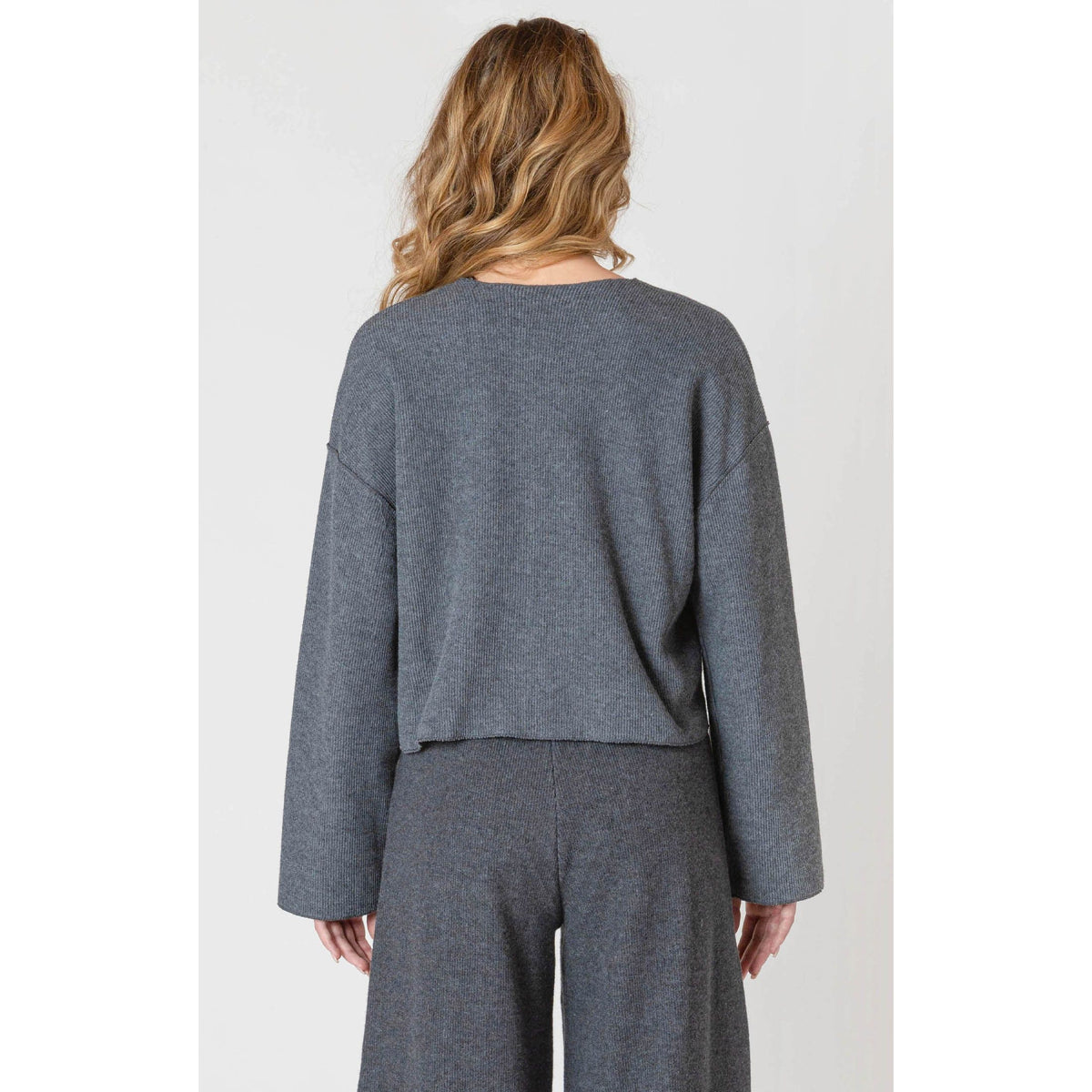 Back view of a model wearing the Room 34 Ribbed Cardigan in gray with long sleeves and a loose fit.