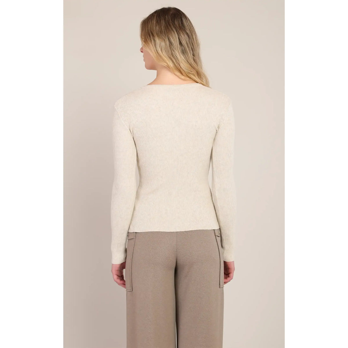 Back view of a cream ribbed V-neck sweater with long sleeves, paired with beige wide-leg trousers.