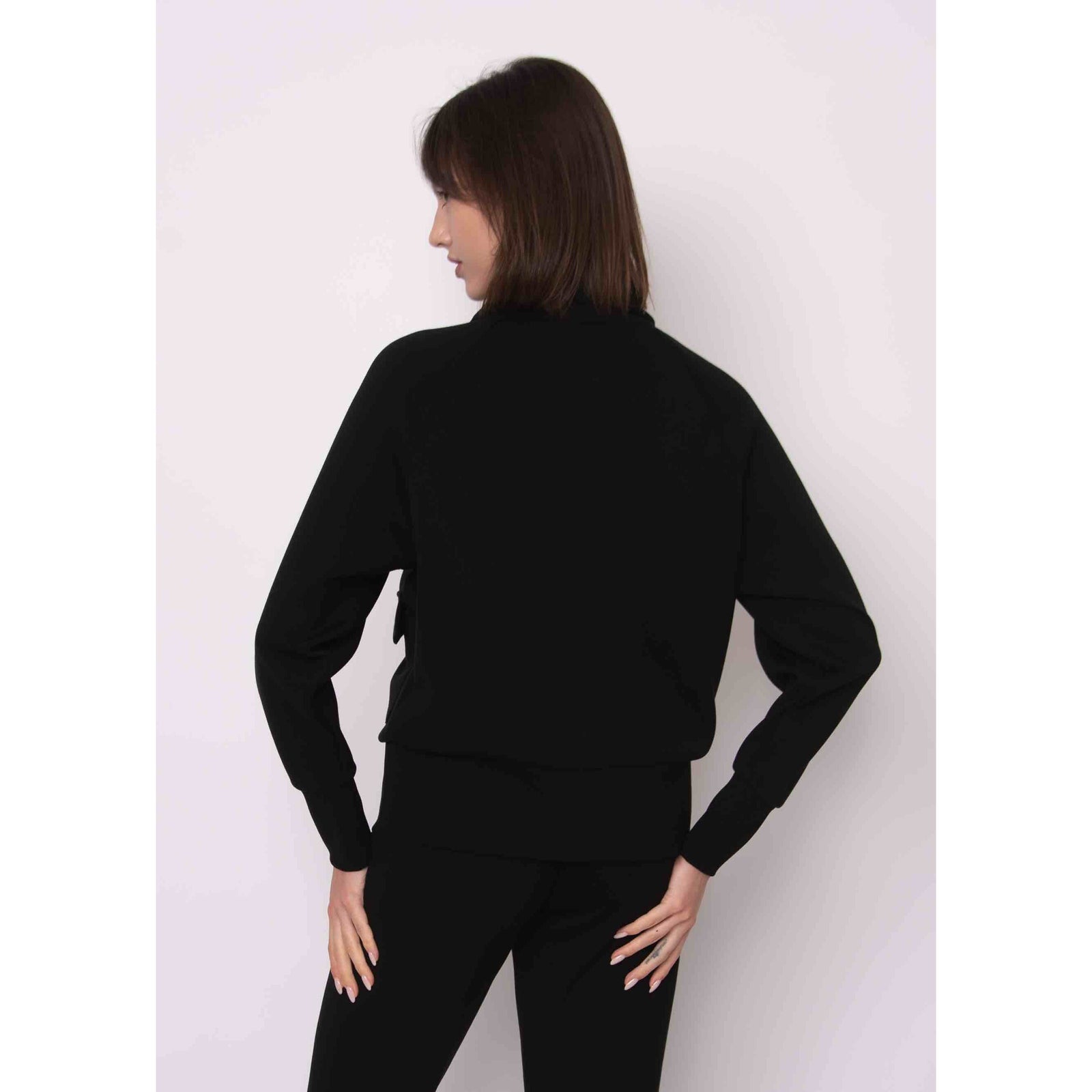 Back view of a model wearing a black Saruna Soft Knit Mock Zip Up with a relaxed fit.