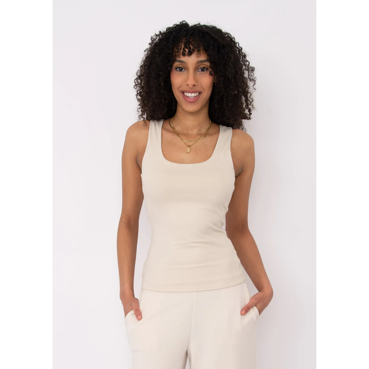 Beige Second Skin Tanith Double Uneck Tank Top on a smiling woman with layered gold necklaces.