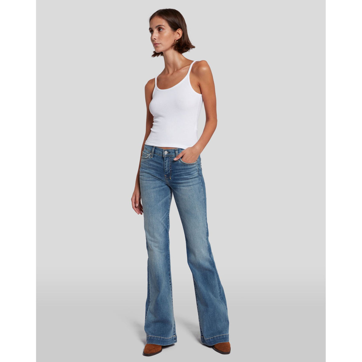 Model wearing 7 for all Mankind Dojo in Slim Illusion jeans, mid-rise flare with a white tank top.