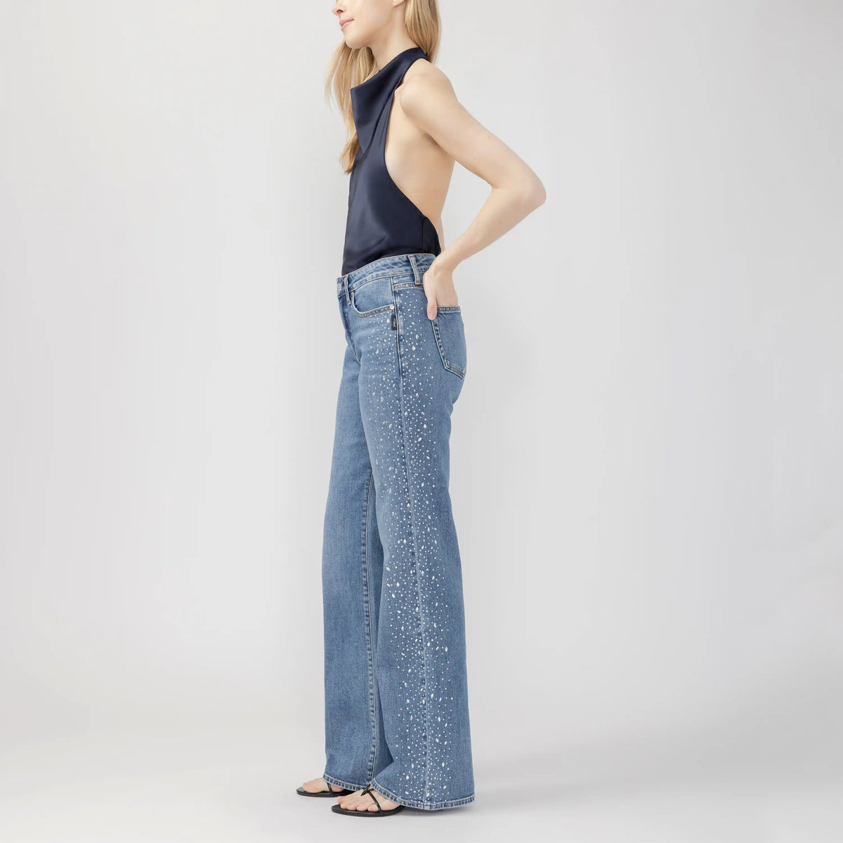 Side view of silver Avery Wildcard trousers featuring a curvy fit, high rise, and speckled white detailing down the wide leg.