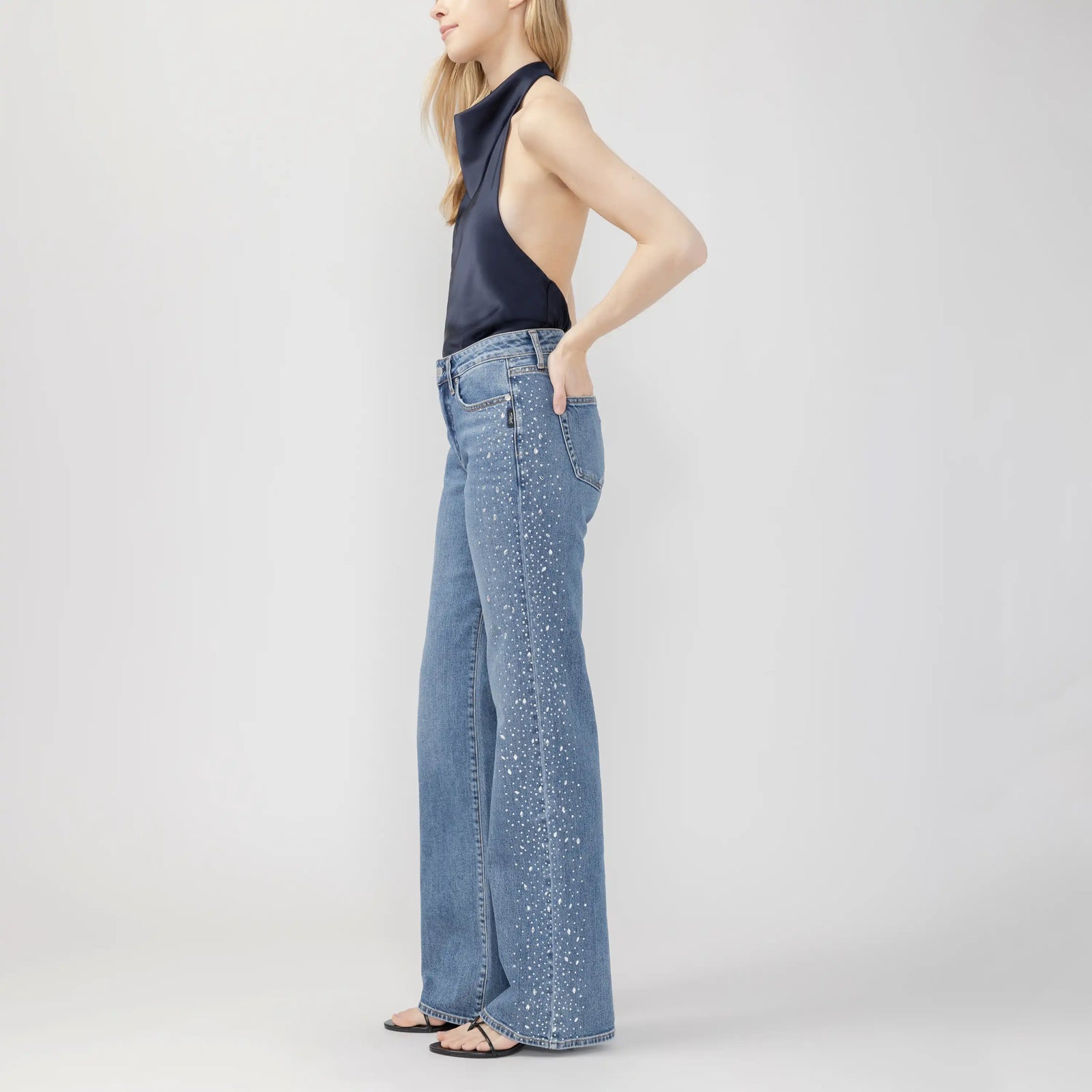 Side view of silver Avery Wildcard trousers featuring a curvy fit, high rise, and speckled white detailing down the wide leg.