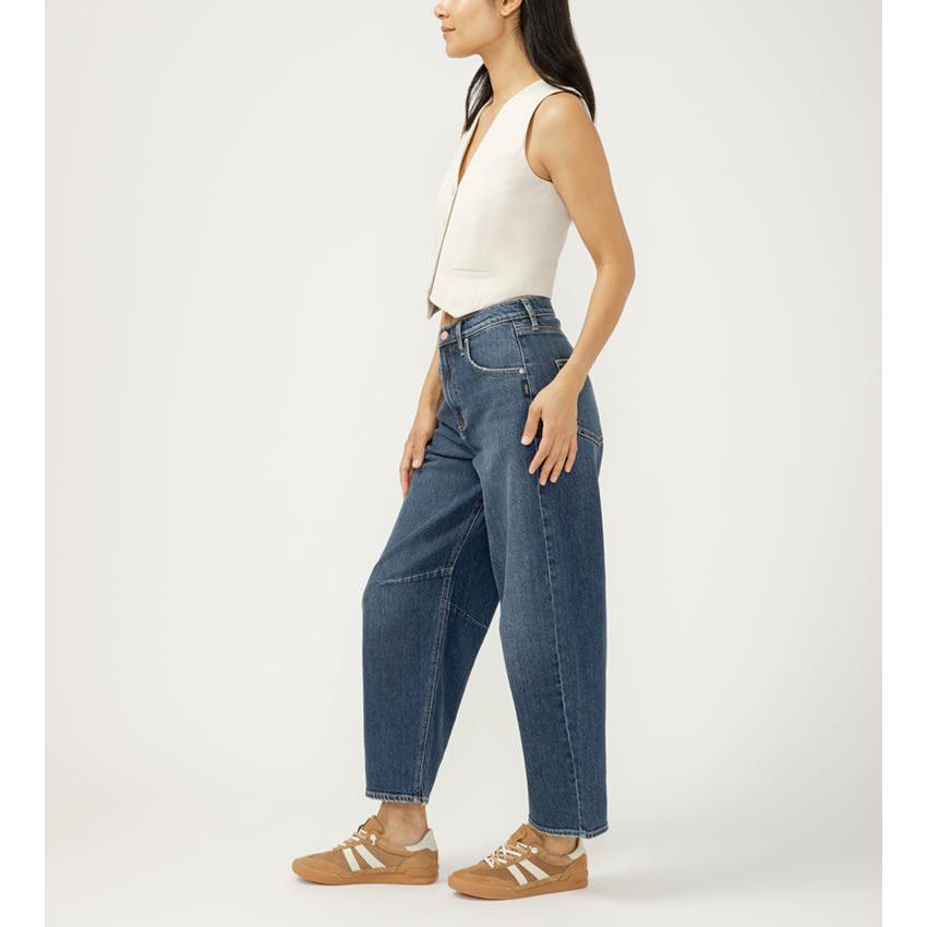 Model in blue high-rise slim barrel-leg jeans with relaxed fit, paired with a white top and tan sneakers.