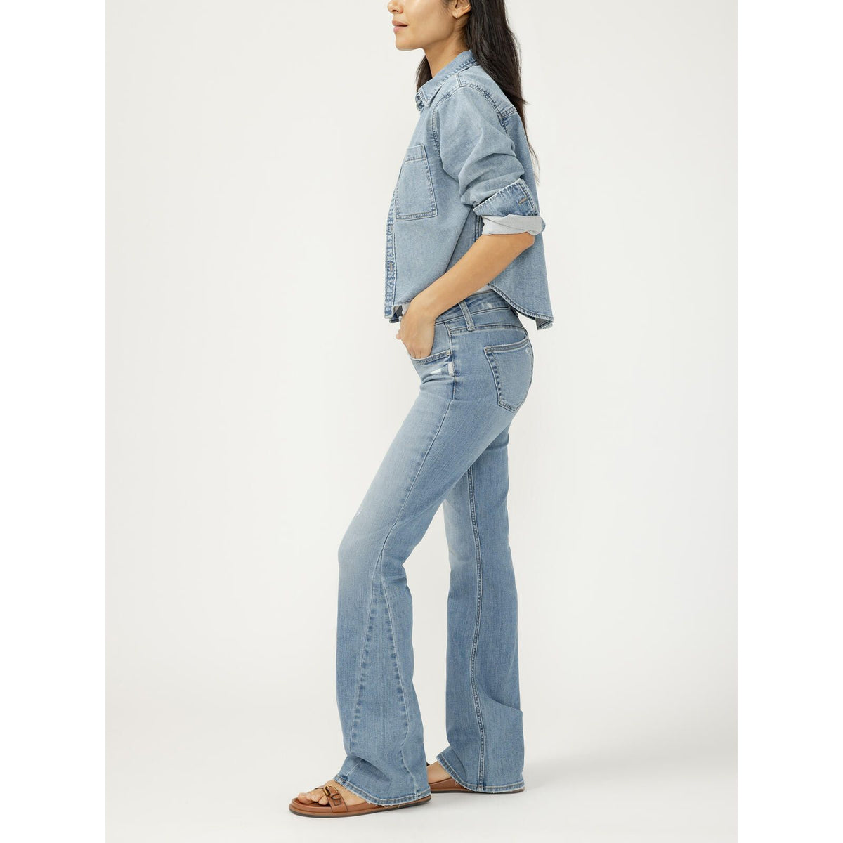 Agic woman in side profile wearing a cropped light wash denim button-up shirt with rolled sleeves and matching flared jeans.