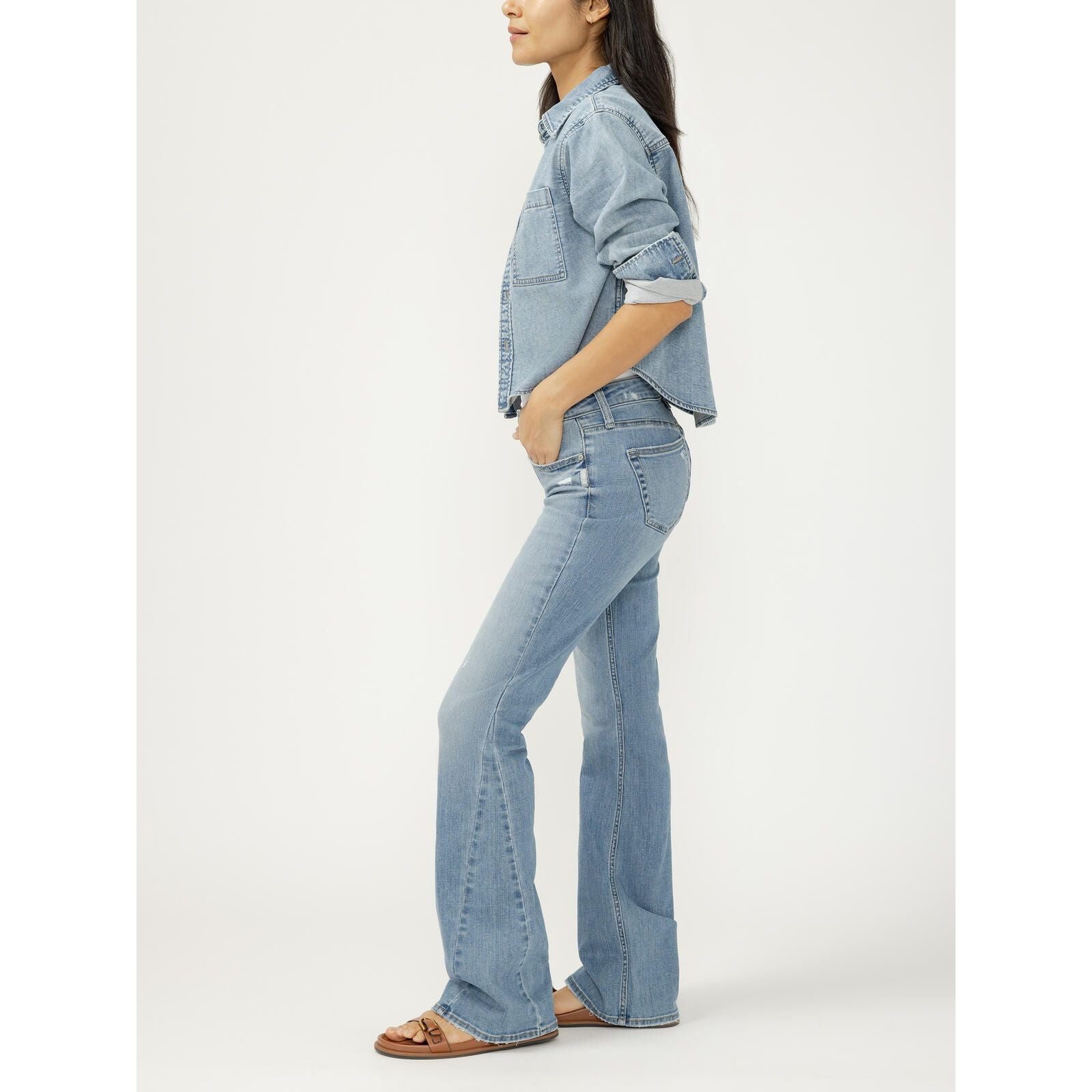 Agic woman in side profile wearing a cropped light wash denim button-up shirt with rolled sleeves and matching flared jeans.