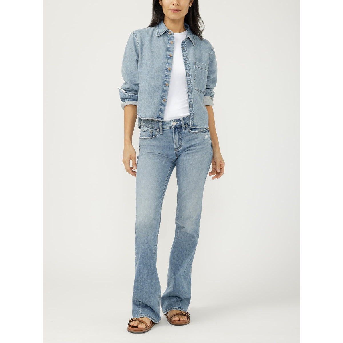 Woman wearing a cropped light wash button front knit flex denim shirt with rolled sleeves over a white tee and matching flare jeans.