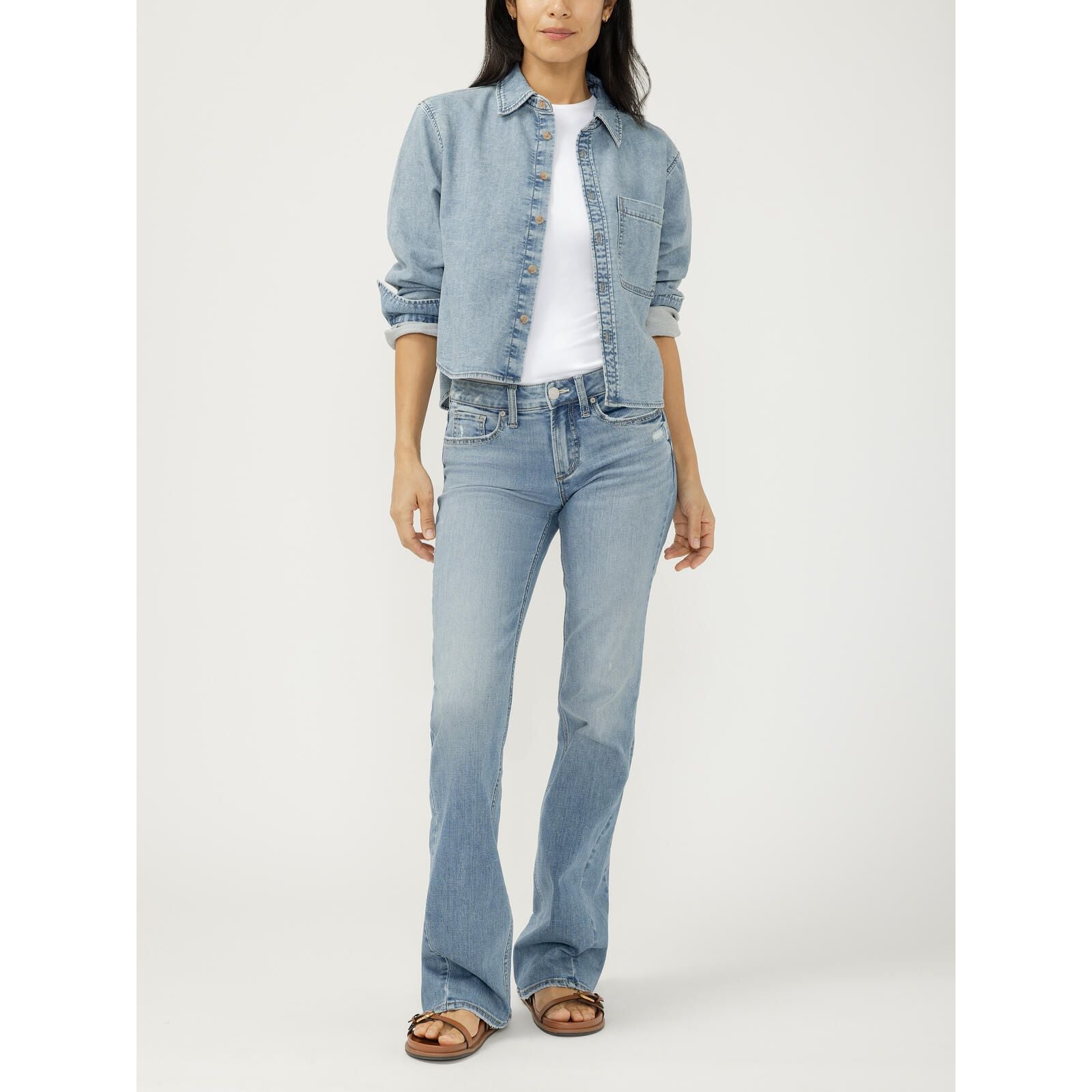Woman wearing a cropped light wash button front knit flex denim shirt with rolled sleeves over a white tee and matching flare jeans.