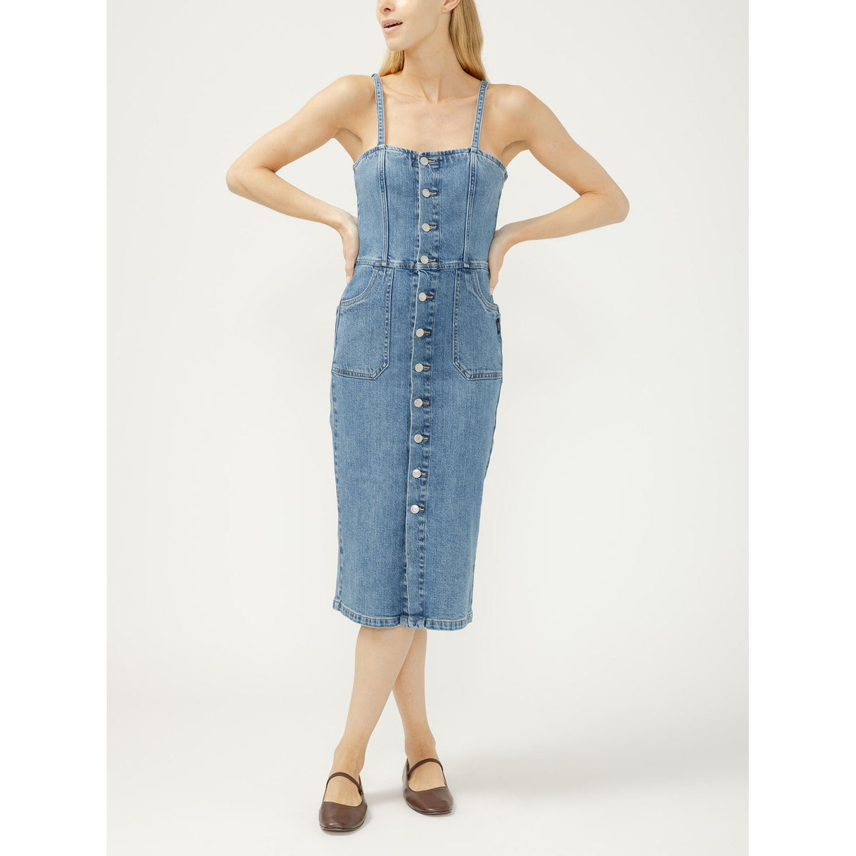 Blue denim midi dress with silver button-front closure, adjustable spaghetti straps, and front pockets on a model.