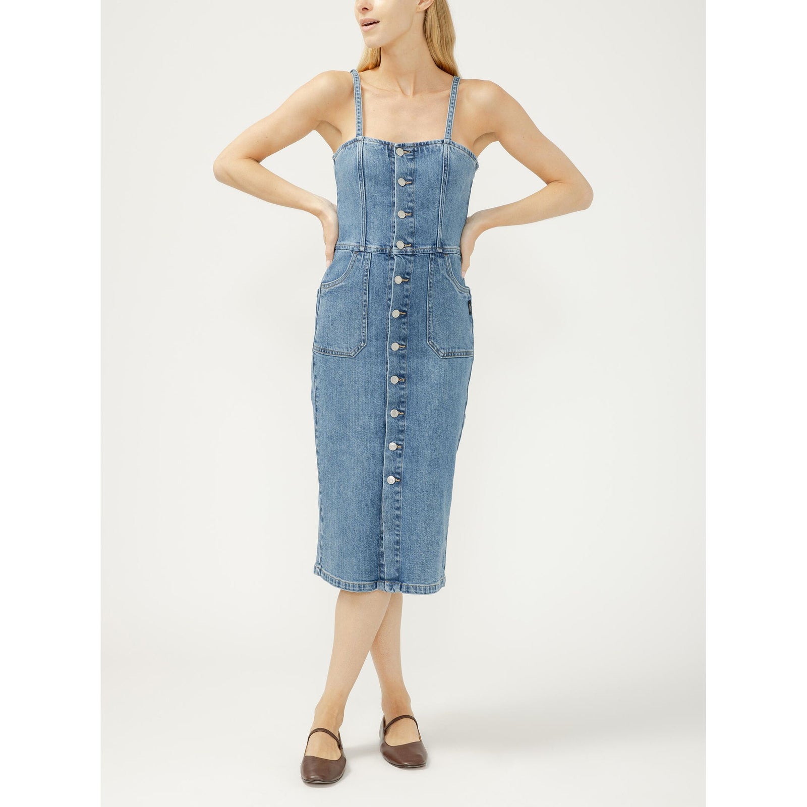 Blue denim midi dress with silver button-front closure, adjustable spaghetti straps, and front pockets on a model.
