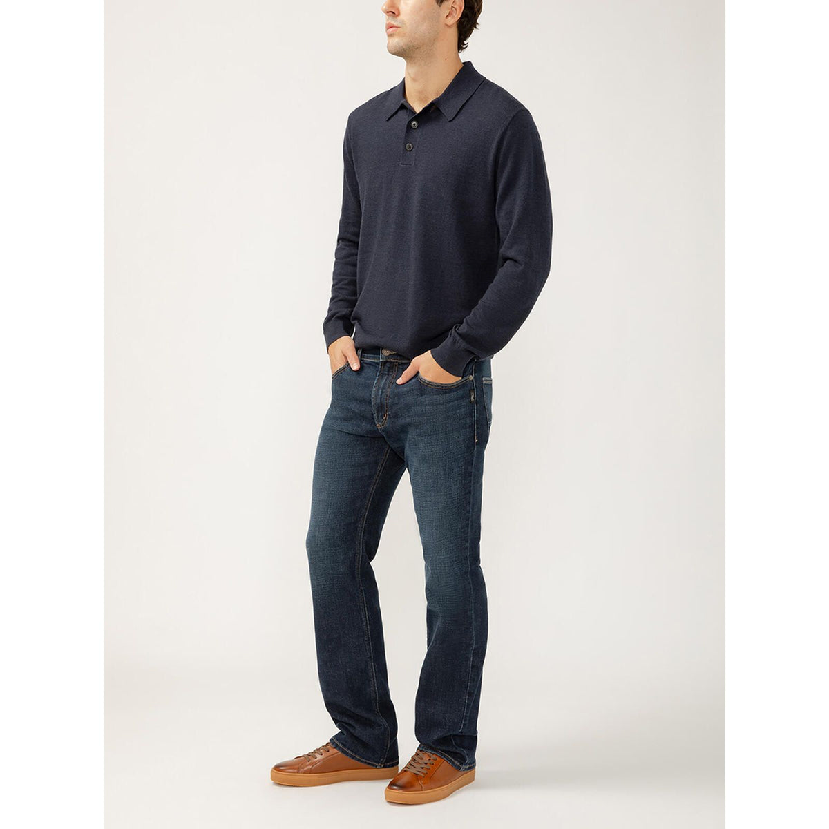 Silver Jace Slim Bootcut Luxe in Swing jeans on a man in a navy knit top with tan sneakers.