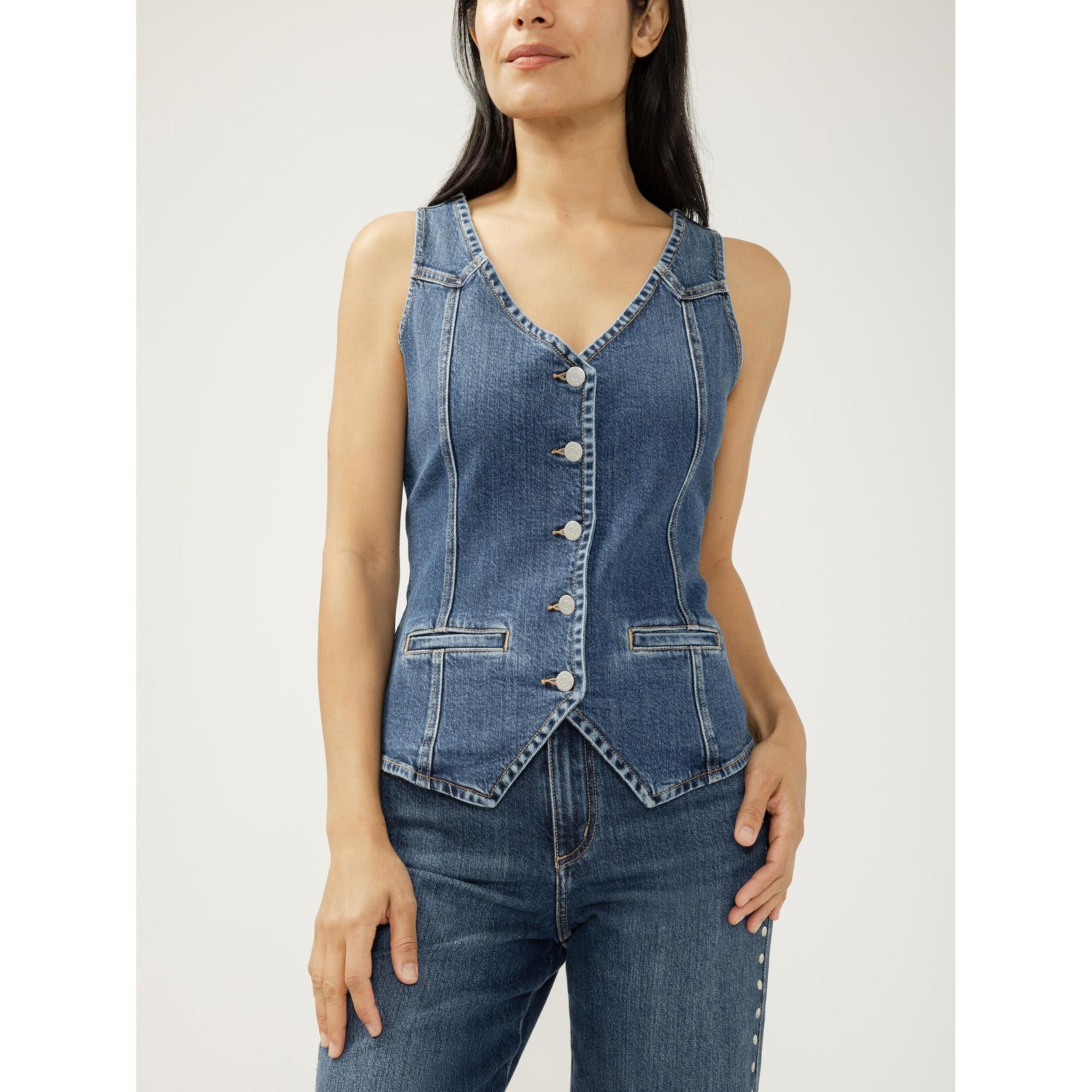 Model wearing a blue denim longline vest with V-neck, button-front closure, front welt pockets, and a pointed hem.