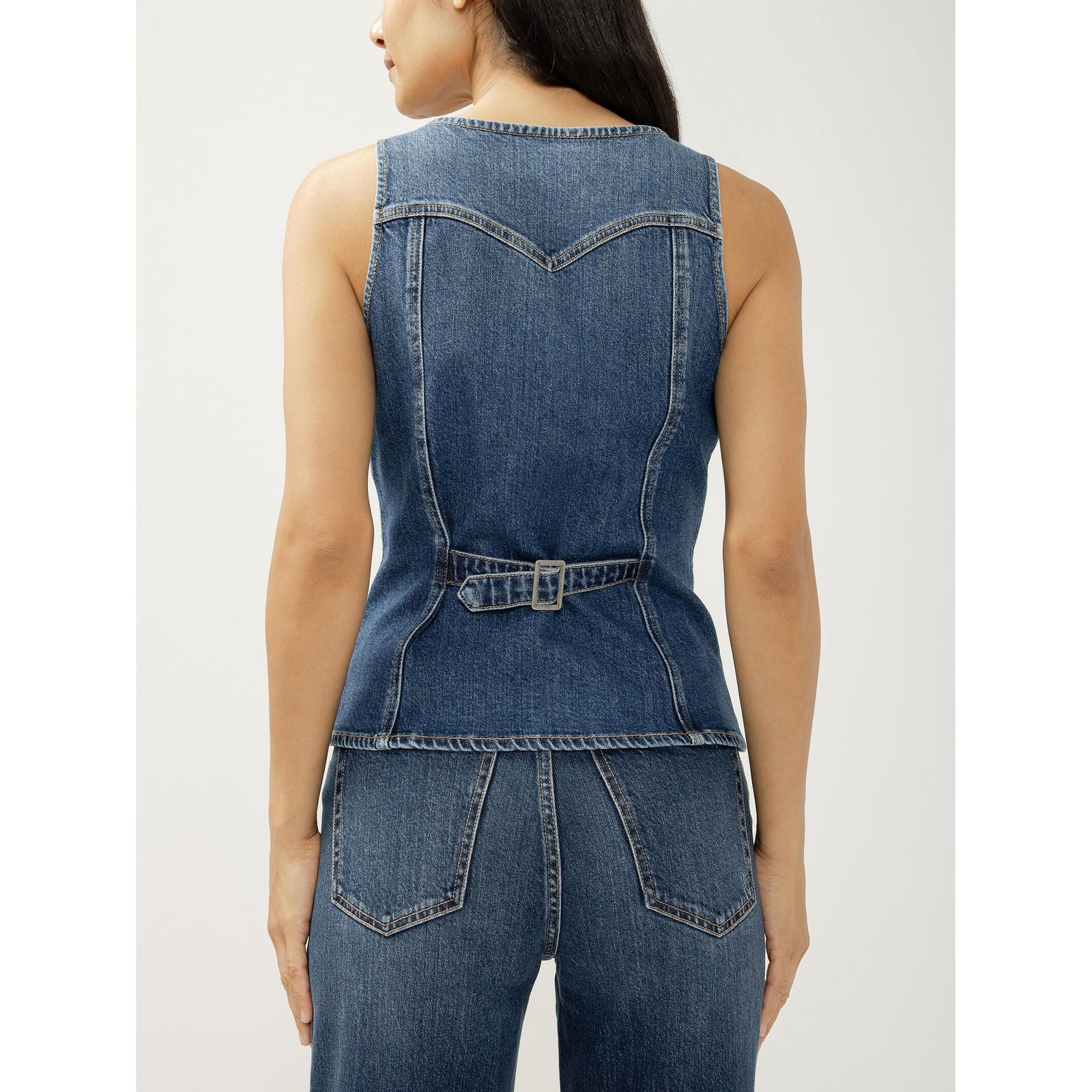 Model wearing a blue denim longline vest with V-neck, button-front closure, front welt pockets, and a pointed hem.