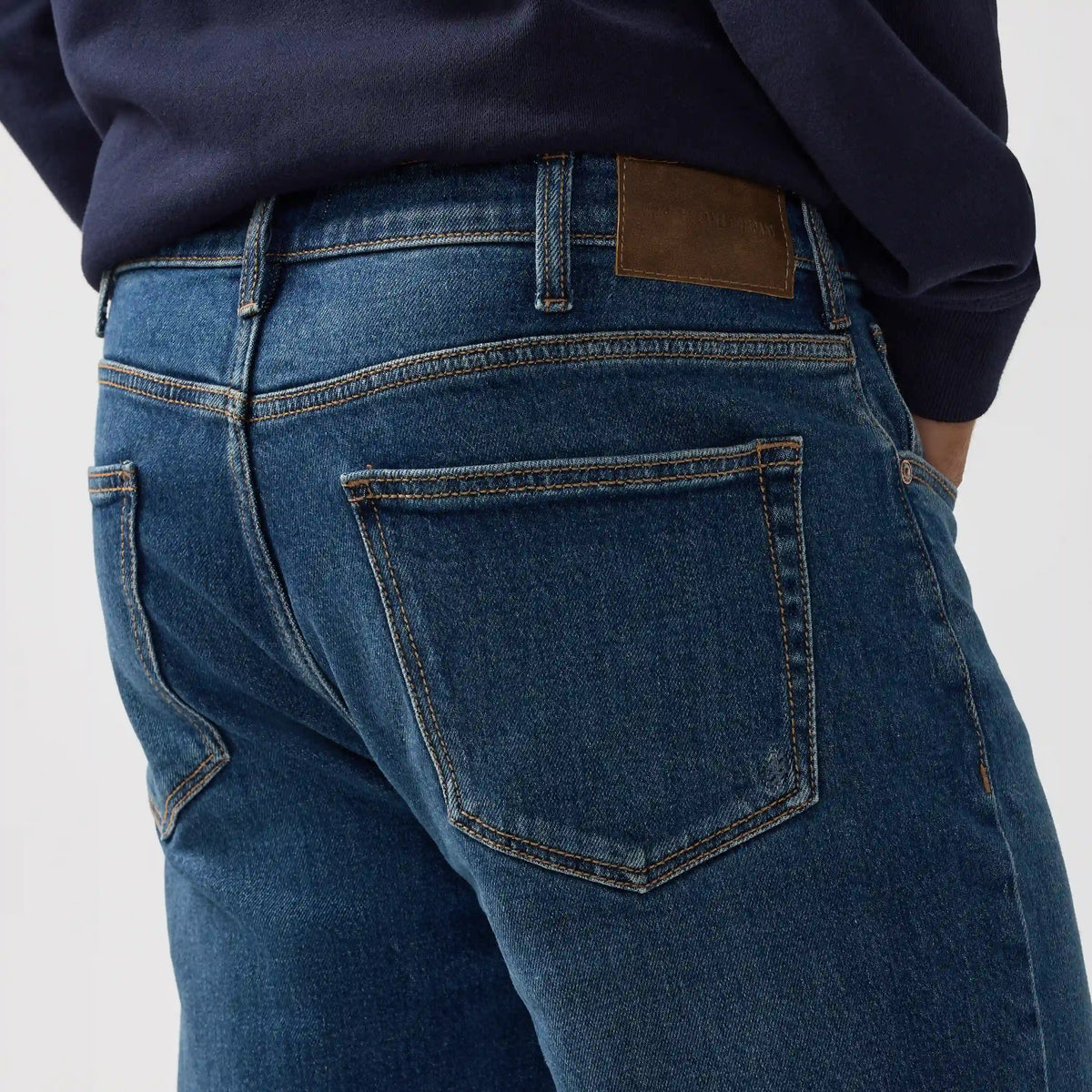 Back view of relaxed straight jeans in Rocky wash. Deep indigo denim with contrast stitching, back pockets, and leather waist patch.
