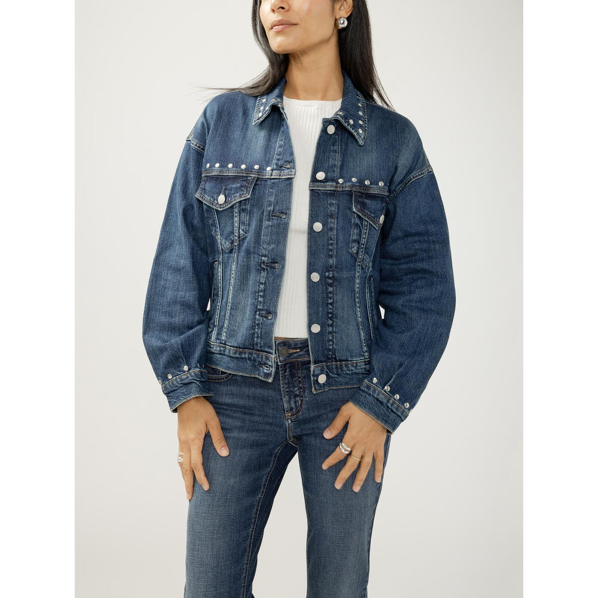 Model wearing a fitted blue denim jacket with silver studs along the collar, yoke, and cuffs.