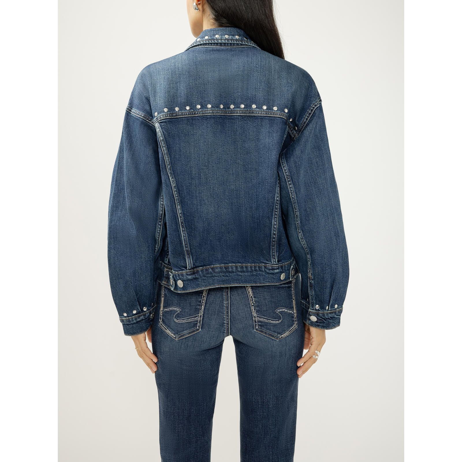 Model wearing a fitted blue denim jacket with silver studs along the collar, yoke, and cuffs.