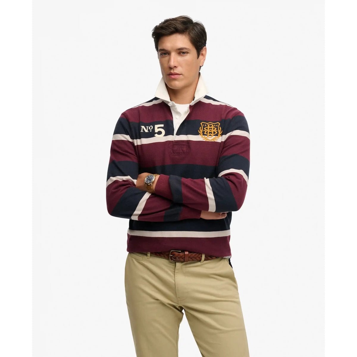 Model wearing Superdry Double Emblem Rugby Shirt with maroon, navy and cream stripes, crest badge and No. 5.
