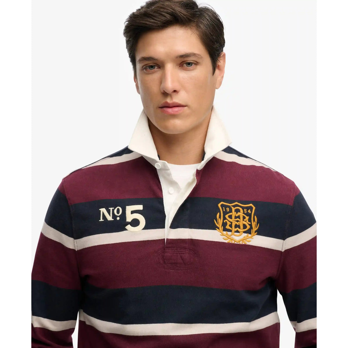 Male model wearing Superdry Double Emblem Rugby Shirt with maroon, navy stripes and crest badge.