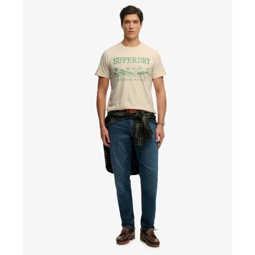 Superdrydry Retro Outdoor Relaxed Tee on model with vintage chest graphic, beige tee and blue jeans.