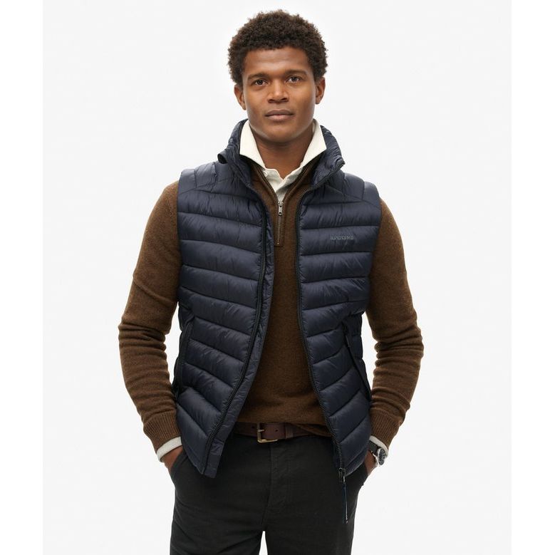 Superdry Fuji Sport Padded Gilet in navy, slim-fit with zip pockets, worn over a brown knit sweater.