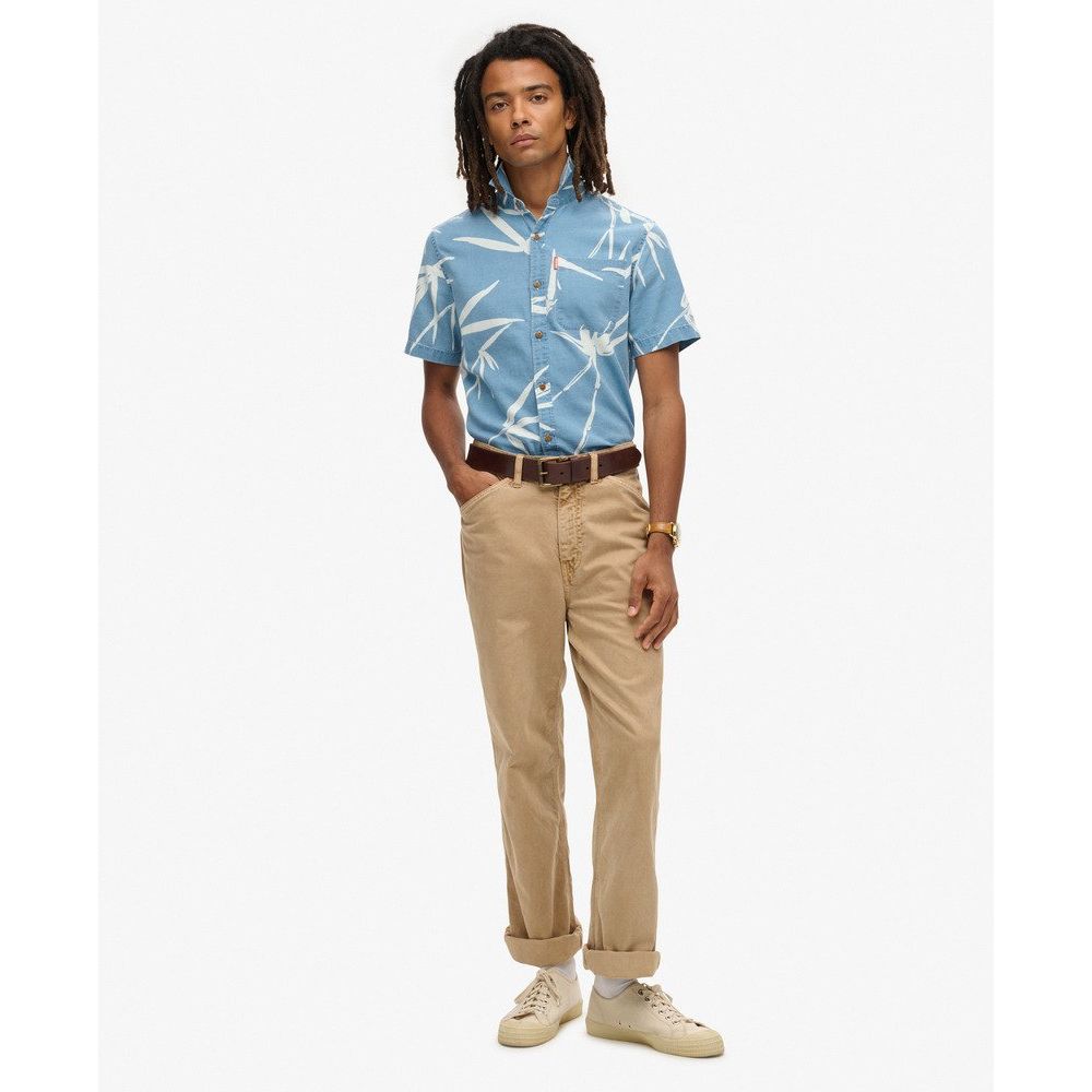 Male model wearing blue Superdry Vintage Loom S/S Shirt with white loom print, tan chinos, and sneakers.