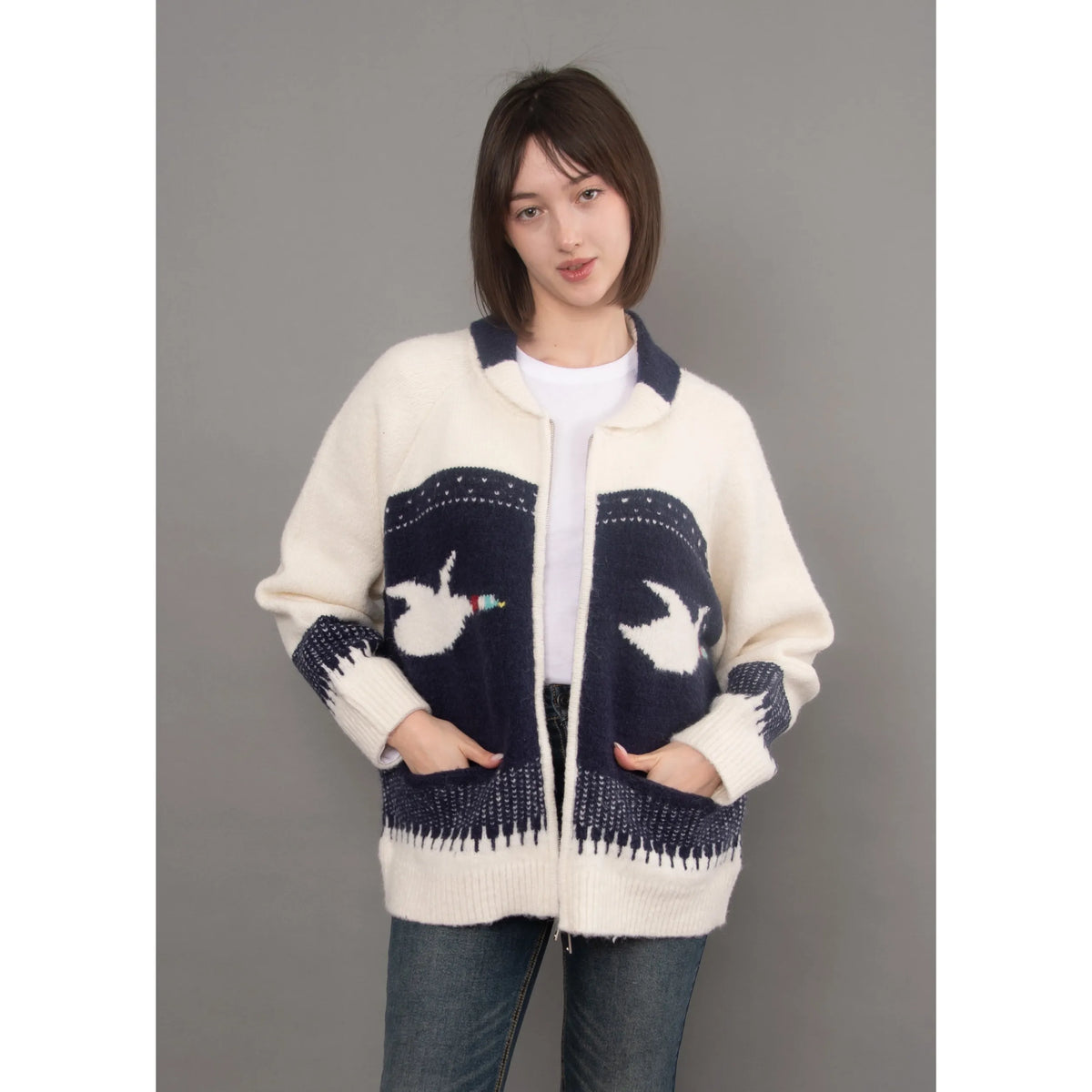 Cream and navy knit cardigan featuring a shawl collar, raglan sleeves, and white bird motifs on the front pockets.