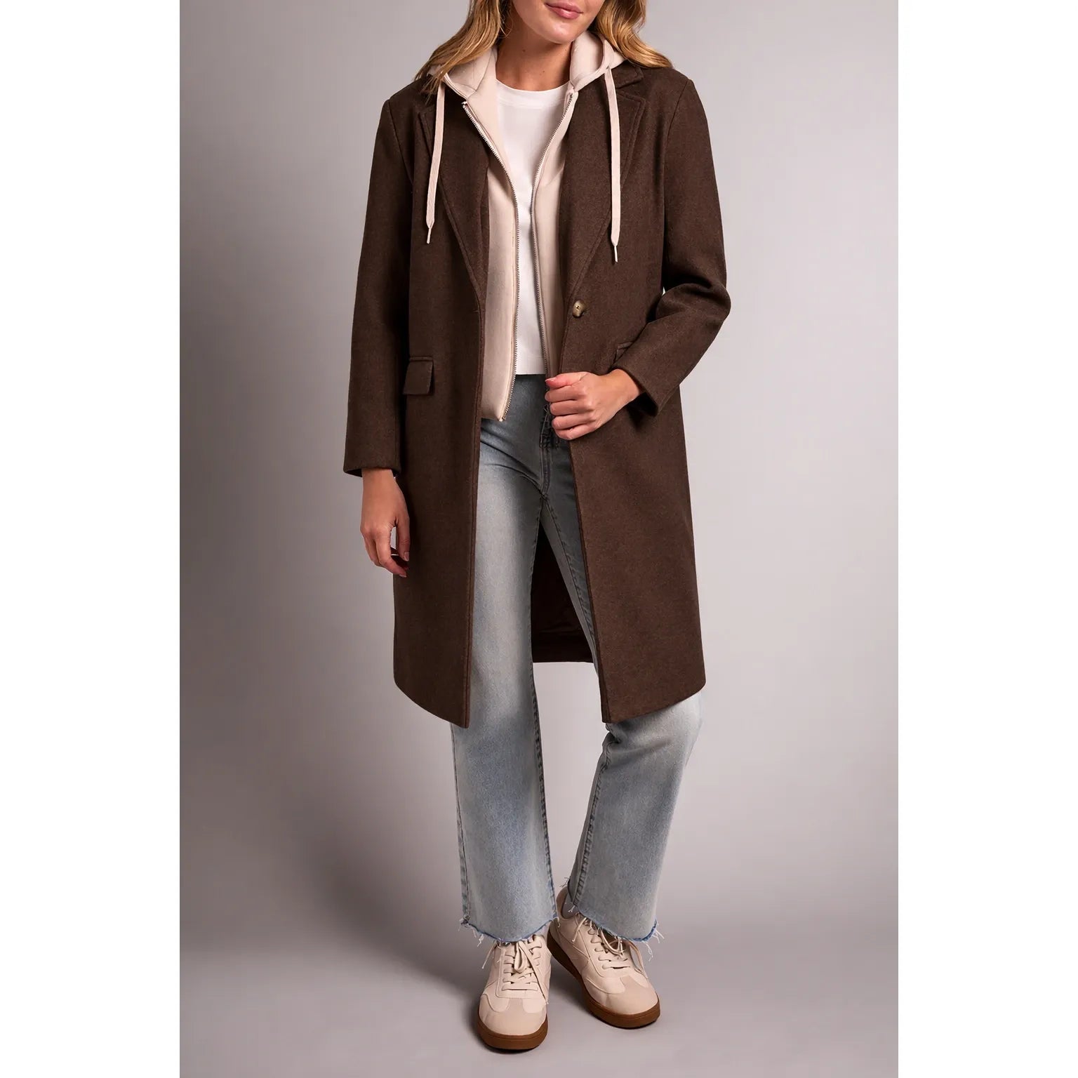 Brown tribal knit car coat with notch lapels and removable beige fooler hoodie insert layered over jeans.