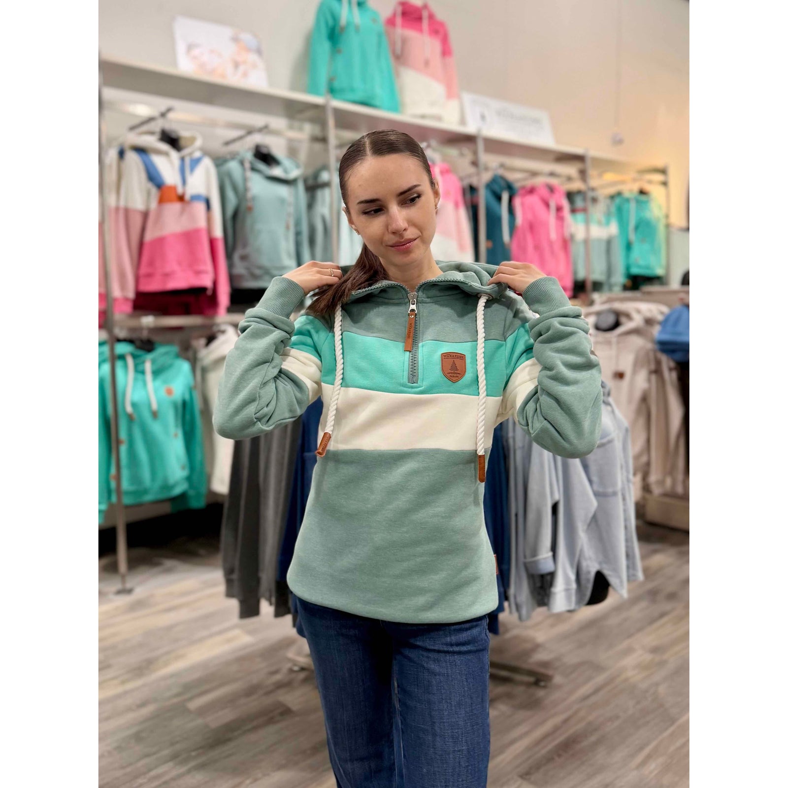 Model wearing Wanakome Further Shores 1/2 Zip Hoodie with teal, mint, and white tri-color blocks, hood and patch.