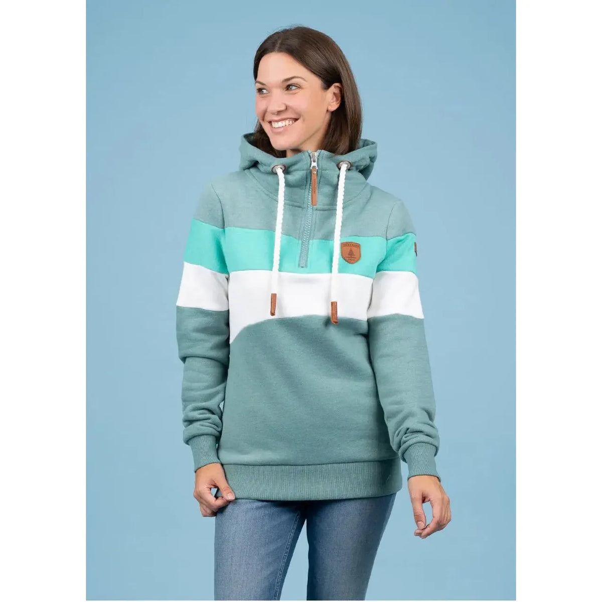 Model wearing Wanakome Further Shores 1/2 Zip Hoodie with teal, mint, and white tri-color blocks, hood and patch.