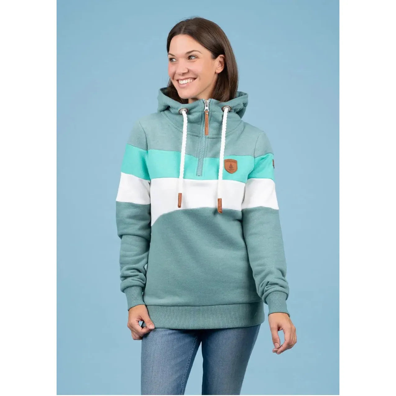 Model wearing Wanakome Further Shores 1/2 Zip Hoodie with teal, mint, and white tri-color blocks, hood and patch.