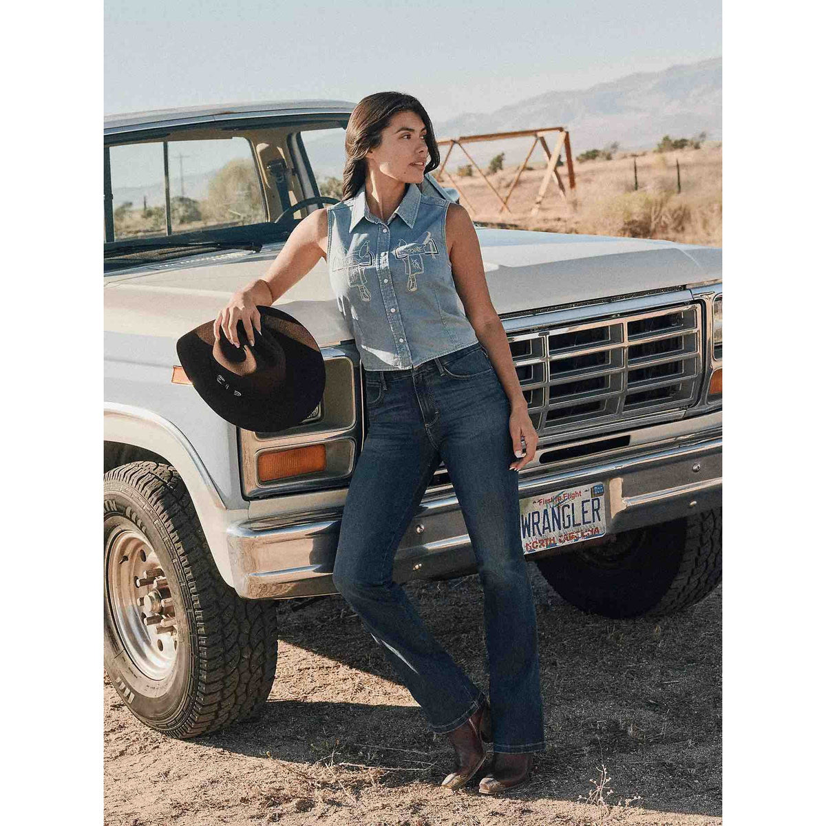 Model wearing Wrangler Bespoke Bootcut in Lacey jeans beside a vintage truck in a desert setting.