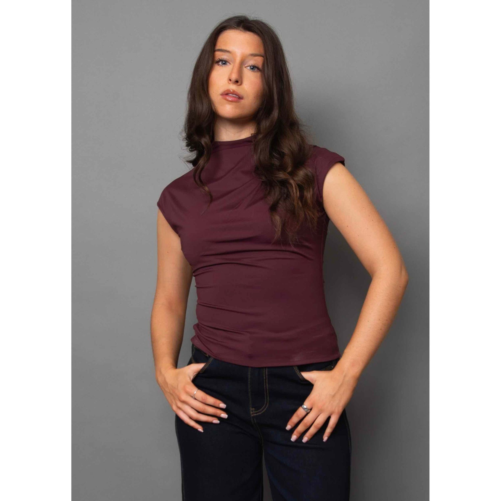 Model wearing burgundy Yvette Funnel Neck Draped Top with sleeveless, draped fit and subtle shoulder pleats.