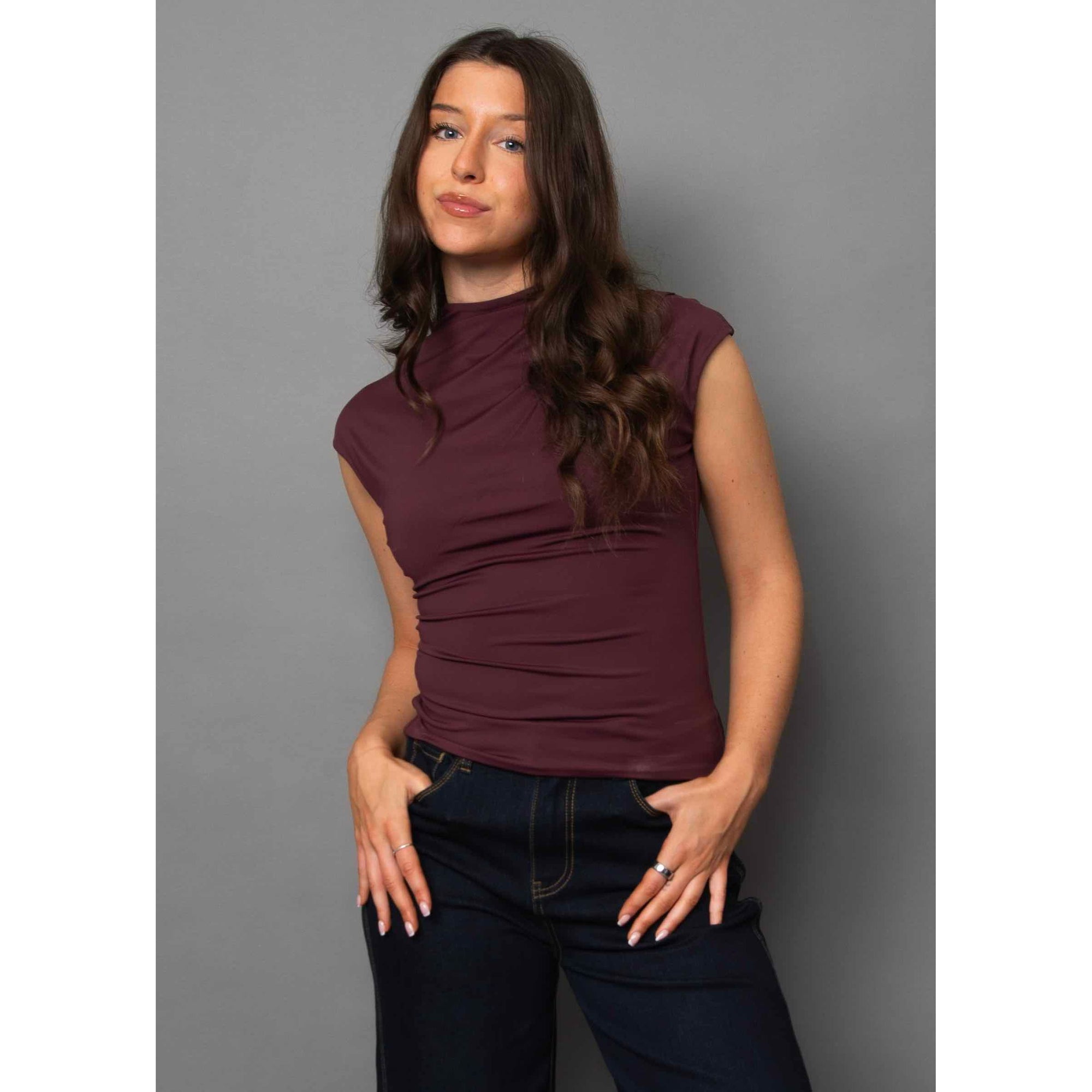 Model wearing Yvette Funnel Neck Draped Top in burgundy, sleeveless with funnel neckline and subtle shoulder pleats.