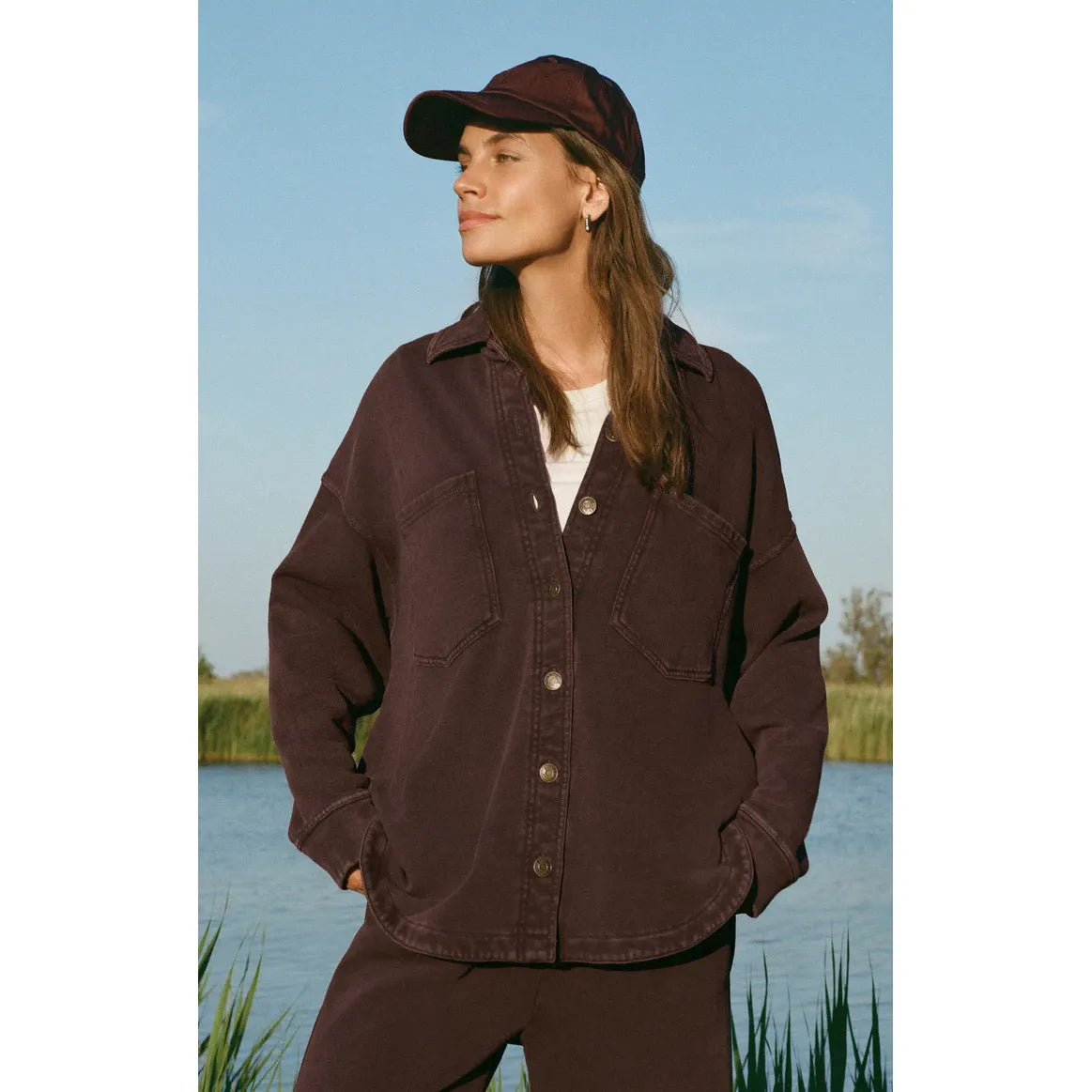 Model wearing Z Supply All Day Knit Jacket in deep brown with large front pockets by a lake, buttery-soft.