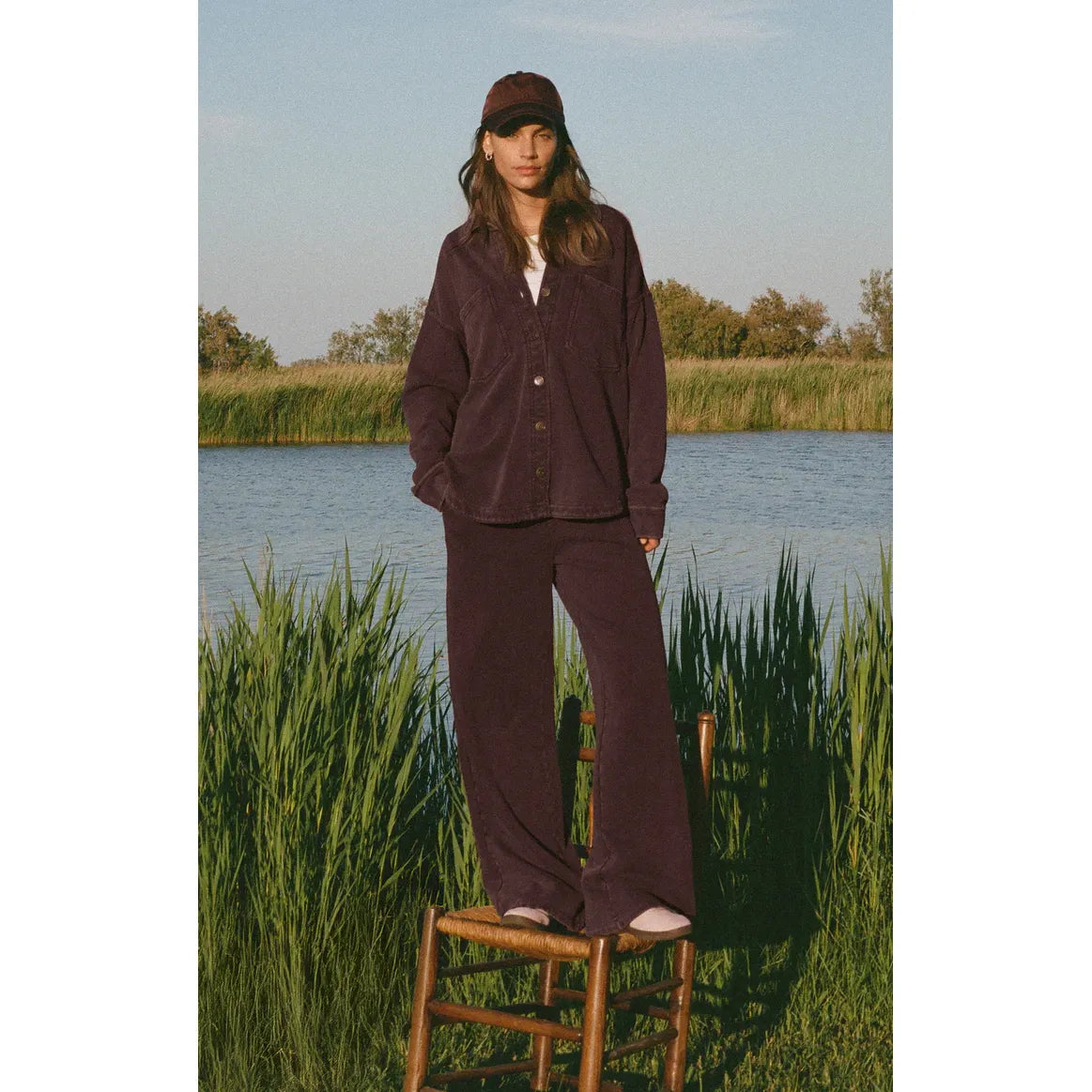 Model wearing Z Supply All Day Knit Jacket in deep brown with large front pockets by a lake, buttery-soft.