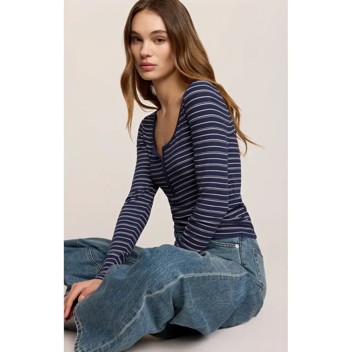 Fitted navy and white striped henley top with long sleeves, scooped neckline, and button placket paired with wide-leg jeans.