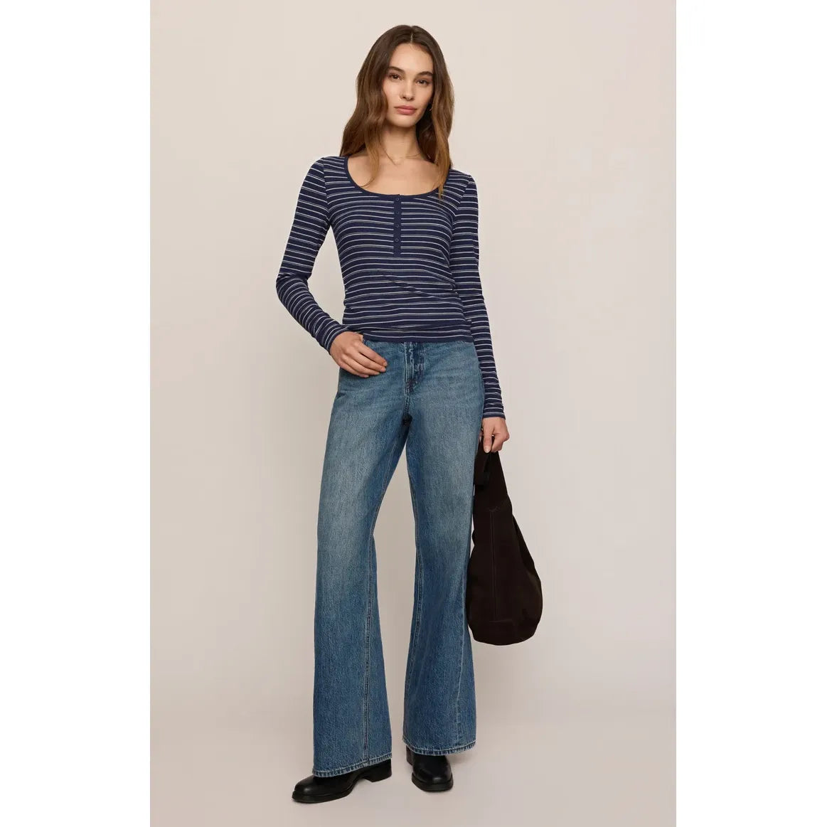 Woman wearing a navy and white striped long sleeve henley with a scooped neckline and button placket, paired with flared jeans.