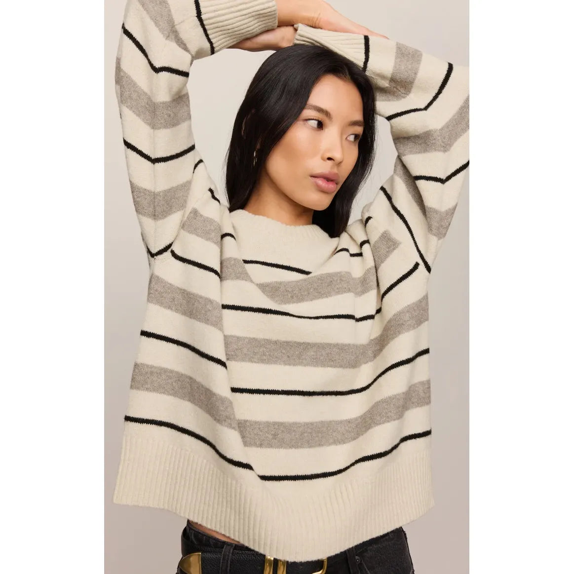 Model wearing a relaxed fit cream and grey striped sweater with thin black lines. Ultra-soft, lightweight knit with a cozy round neckline and ribbed cuffs.