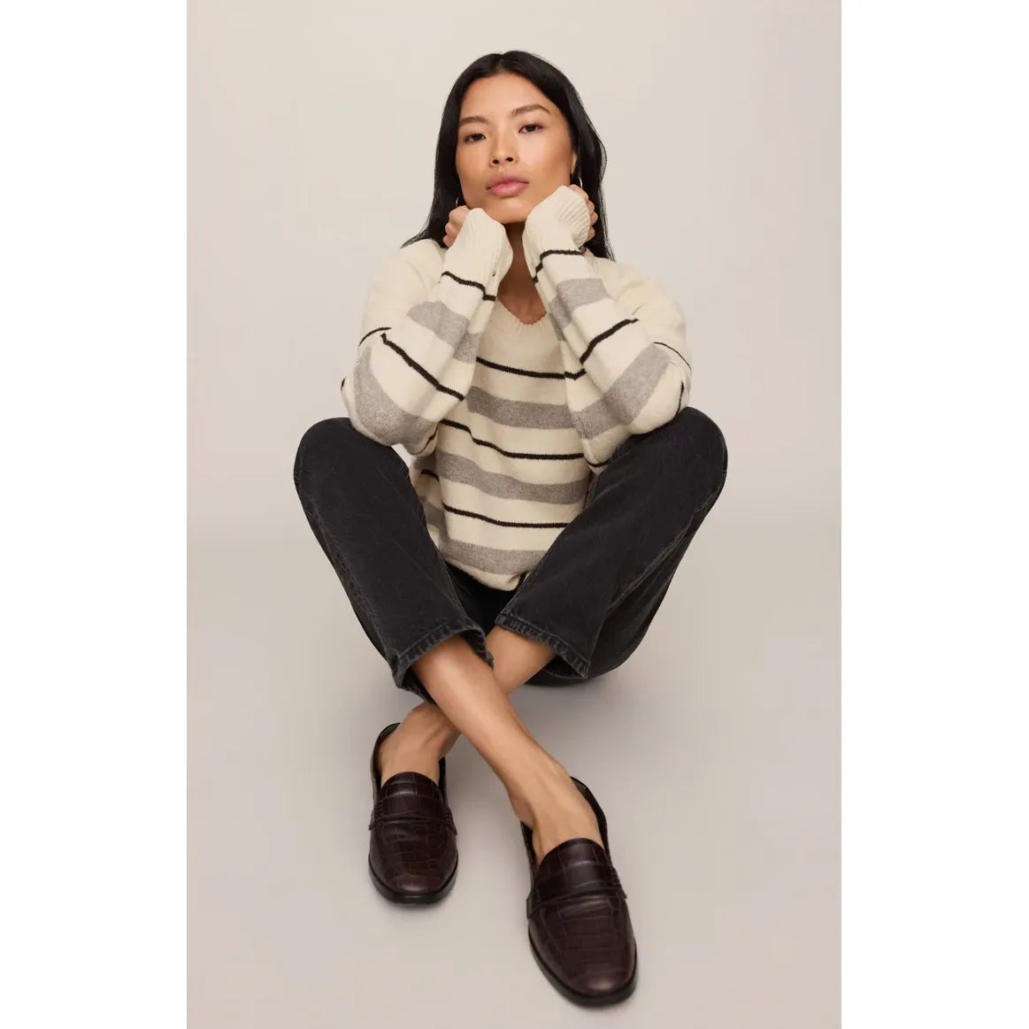 Model wearing a cream and grey striped relaxed fit sweater with dark jeans and brown loafers.