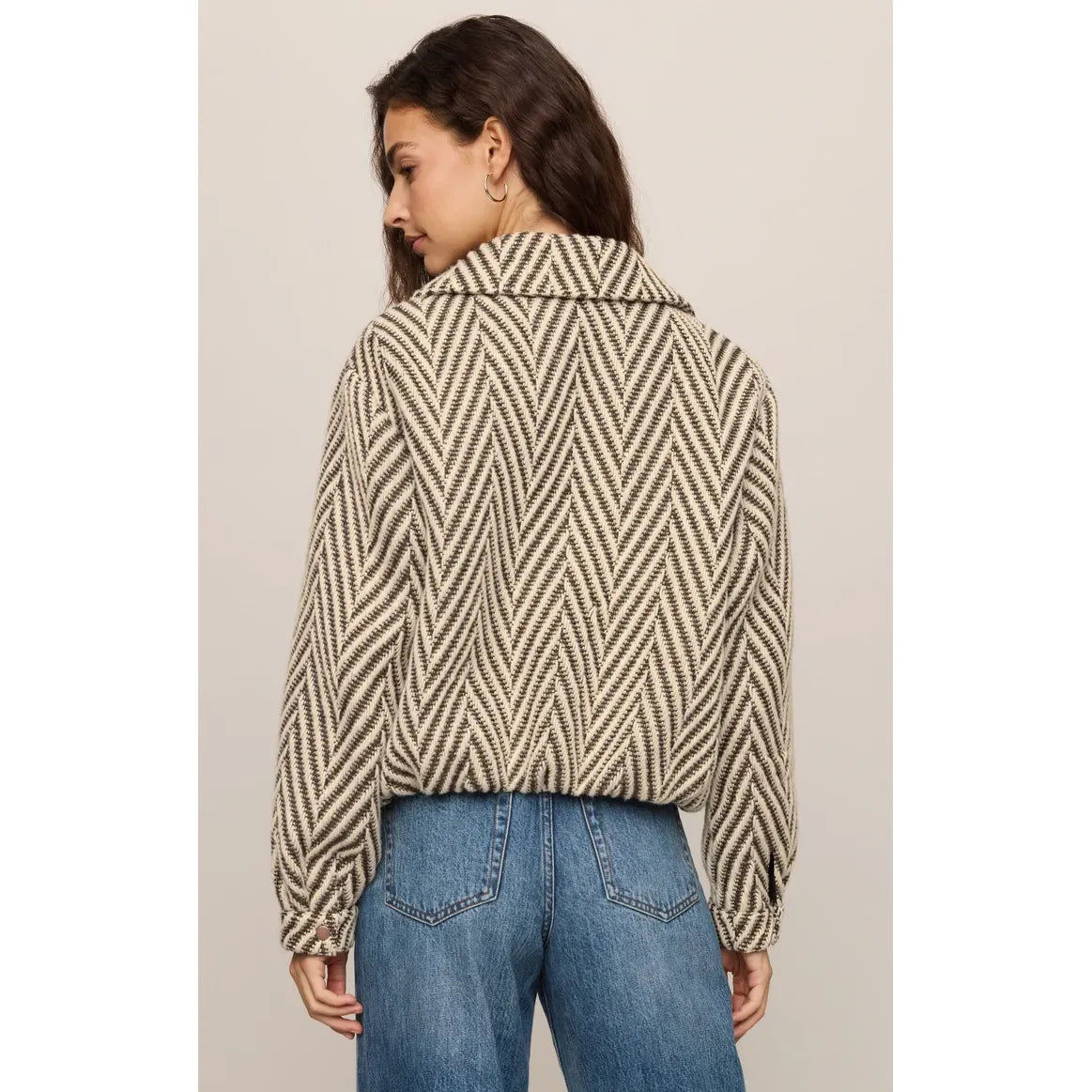 Back view of a cream and brown herringbone bubble jacket with snap cuffs, worn with blue jeans.