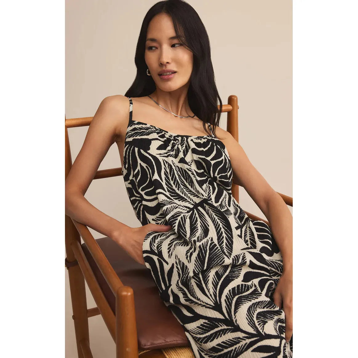 Model lounging in a gauze, black-and-cream tropical print Z Supply Flared Palm Jumpsuit with wide-leg silhouette