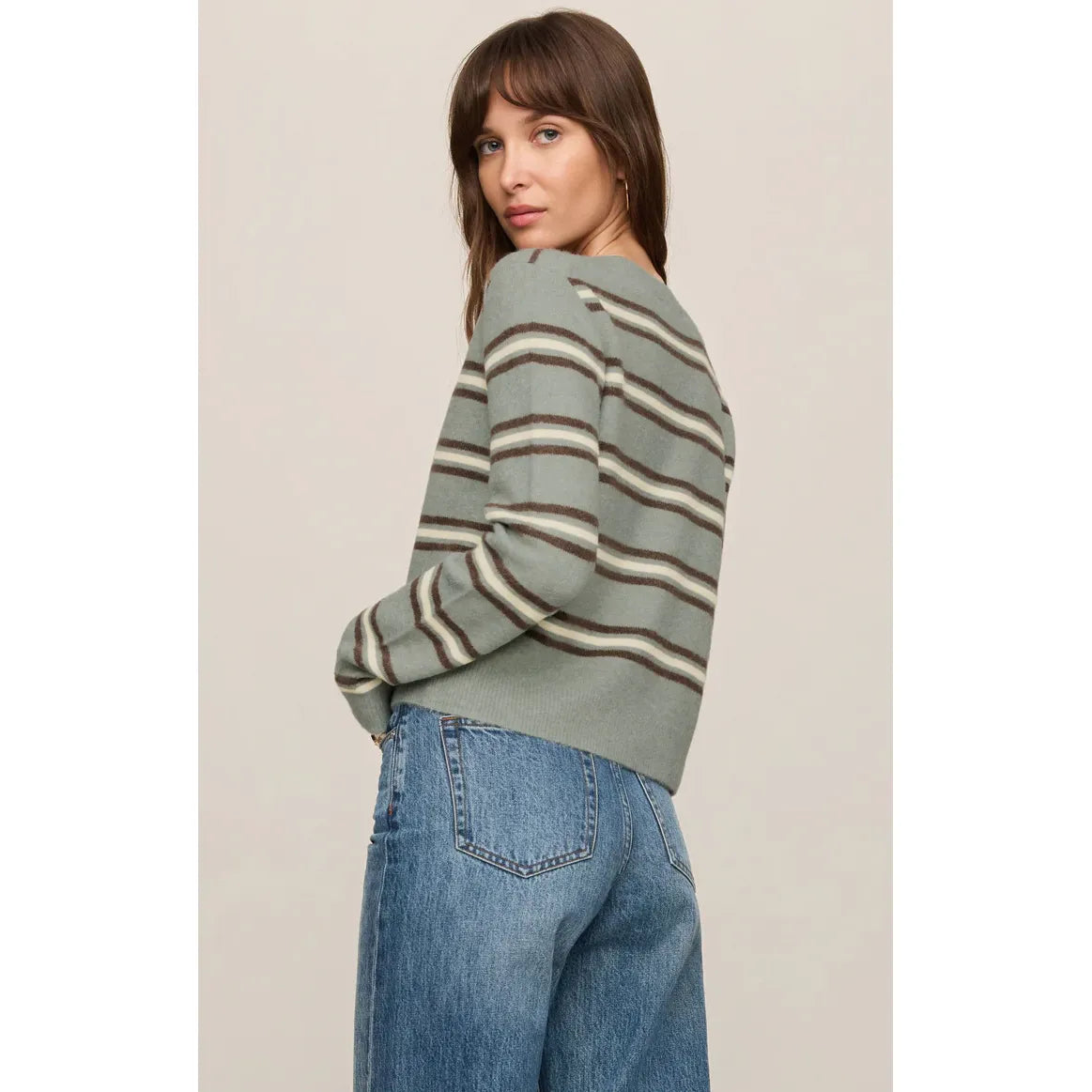 Back view of a woman wearing a sage green retro-striped cardigan with brown and cream horizontal stripes, paired with blue denim jeans.