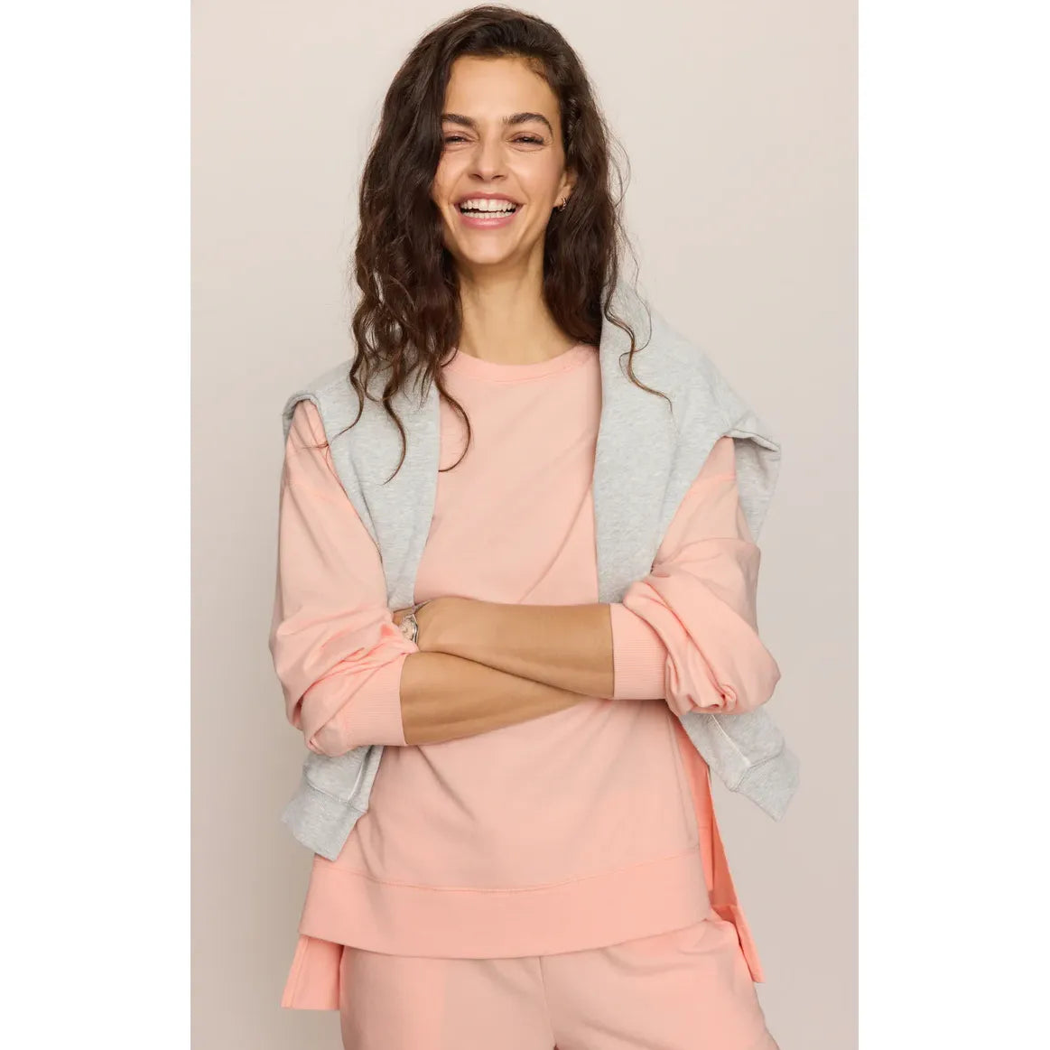 Smiling model wearing peach Z Supply Modern Weekender Sweatshirt with a gray sweatshirt draped over shoulders.