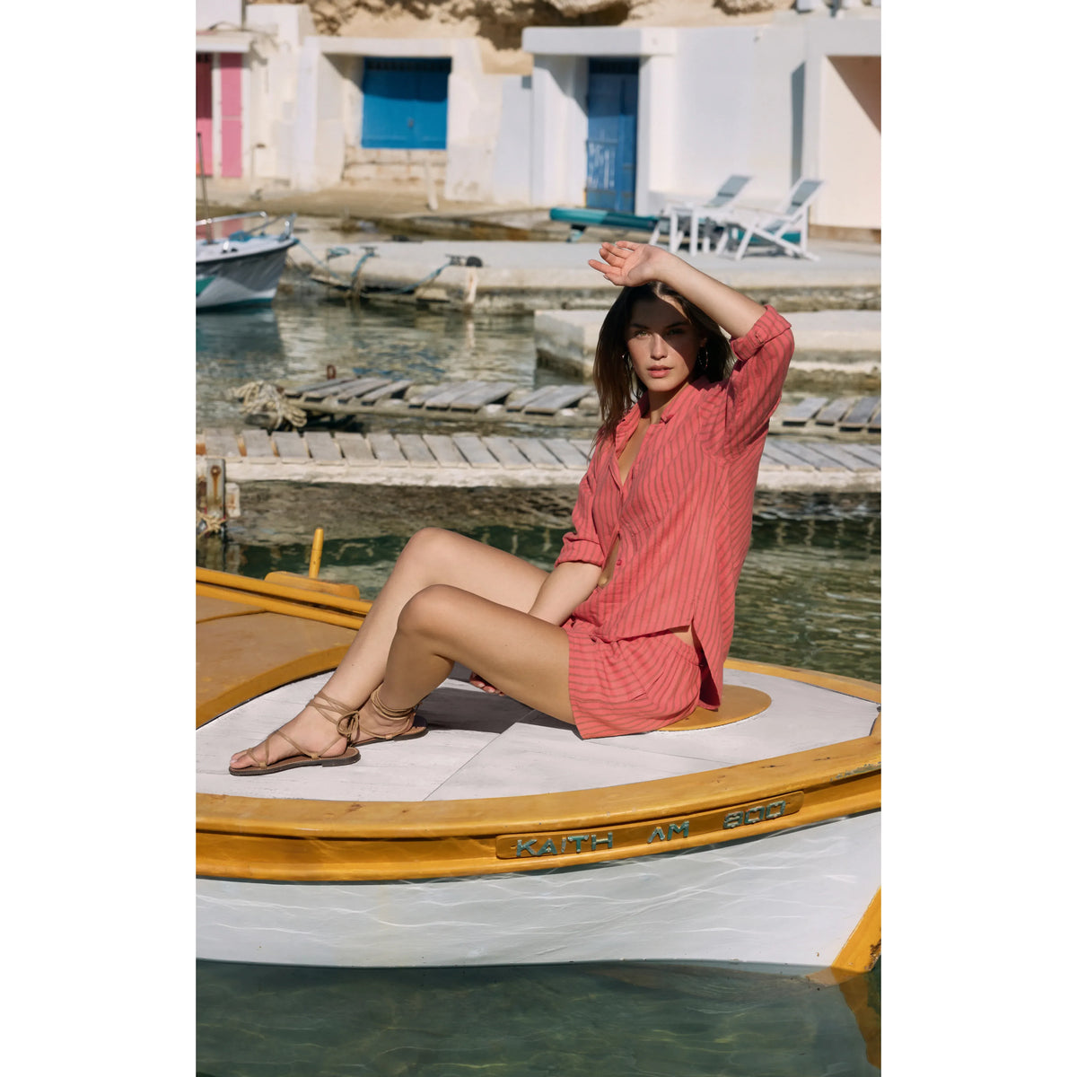 Woman wearing Z Supply Perfect Striped Button Up Top in coral stripes, sitting on a yellow boat by the water.